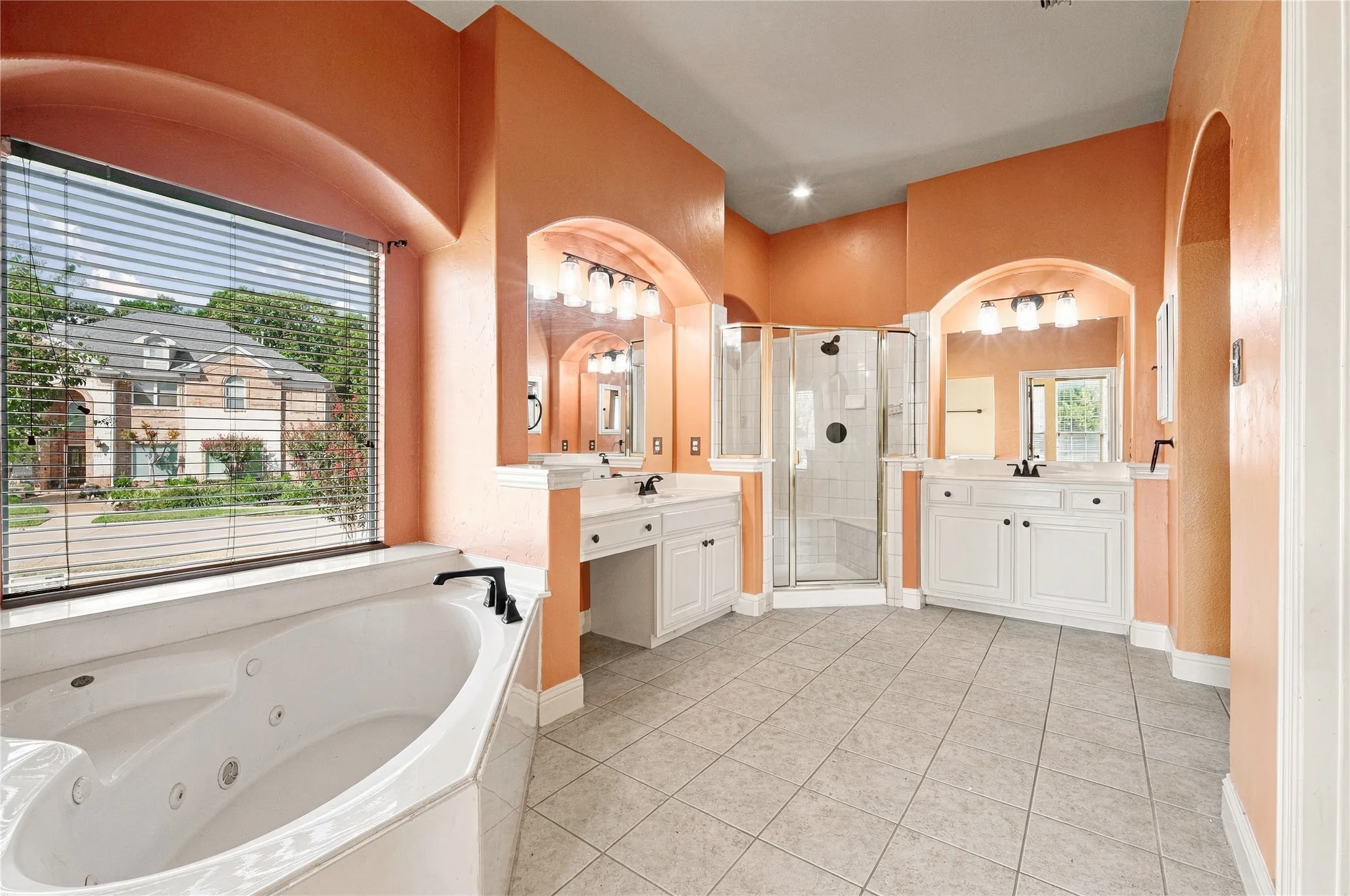 Corner jetted tub, dual vanity sinks, arched architectural details, walk-in shower with glass enclosure, and tile flooring