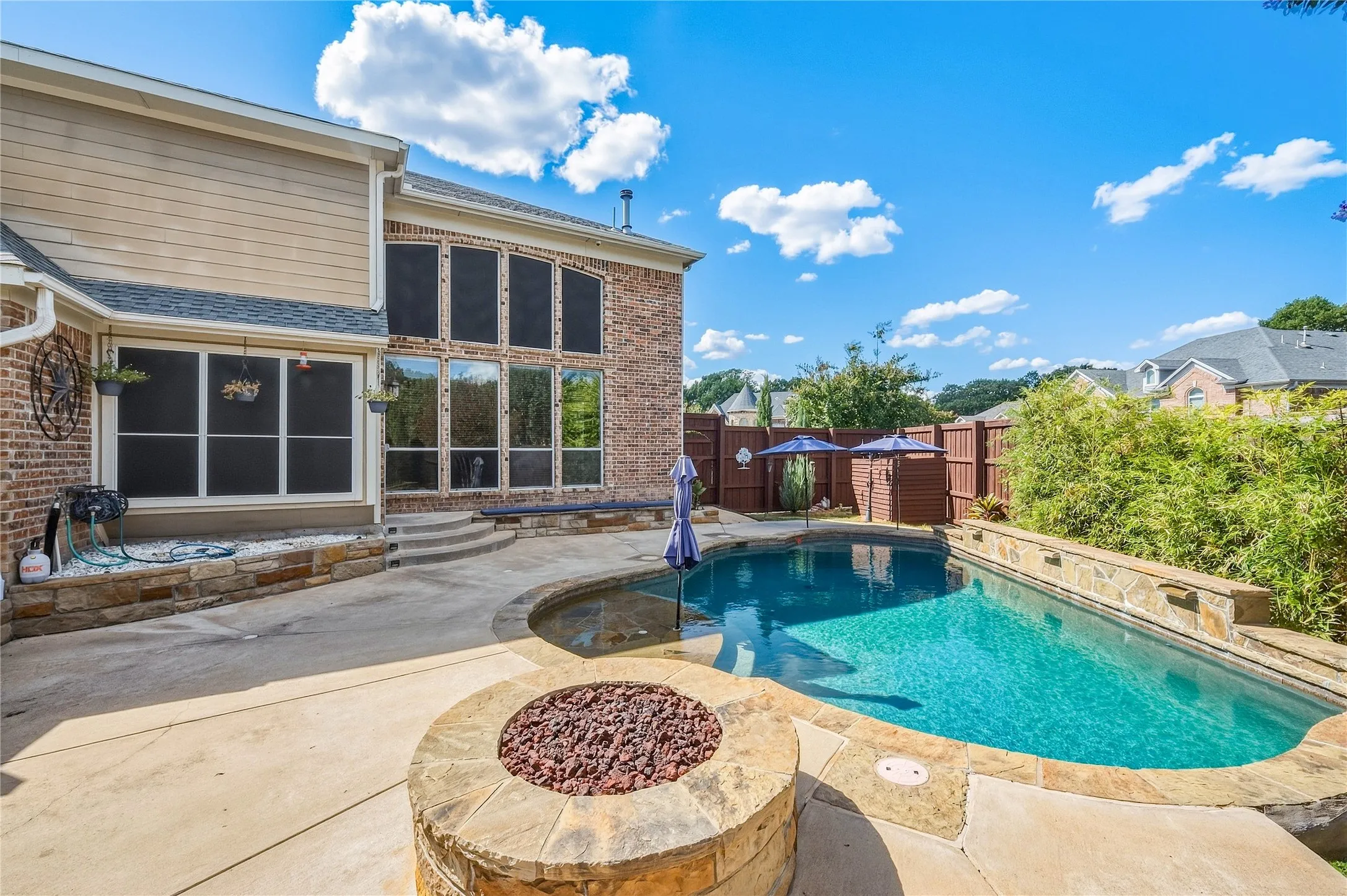 Brick and siding exterior with multiple large windows, an integrated swimming pool, a raised spa, and a stone-clad fire pit