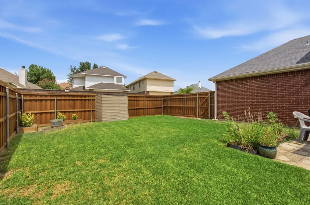 Expansive fenced backyard featuring a grassy lawn, a storage shed, and a paved patio area