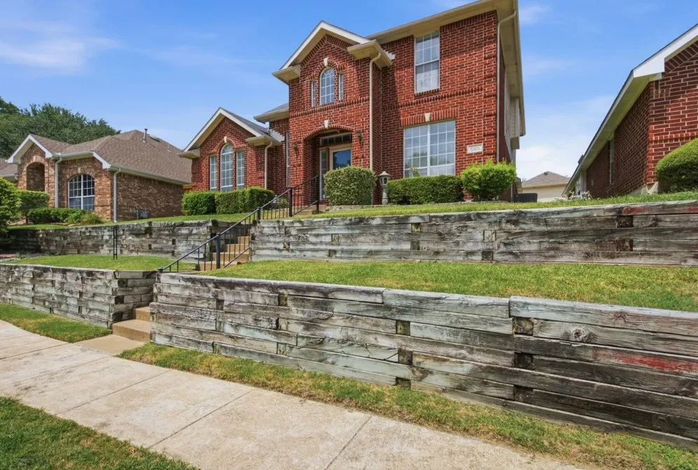 Traditional brick exterior with an arched entryway, multiple windows, and a multi-tiered retaining wall system