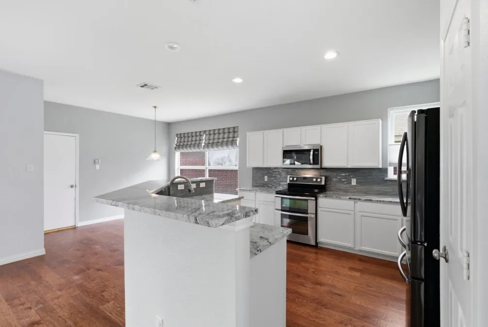 Kitchen featuring wood-finish flooring, white cabinetry, stainless steel appliances, a kitchen island with a built-in sink, and a light-toned backsplash