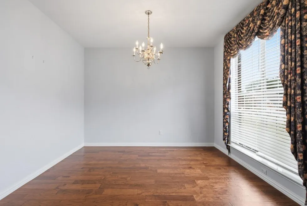 Wood-finish flooring with a decorative chandelier and large window featuring blinds