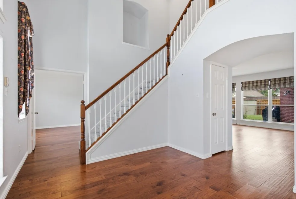Wood-finish flooring, staircase with wood handrail and white balusters, arched entryway, high ceilings, and large windows