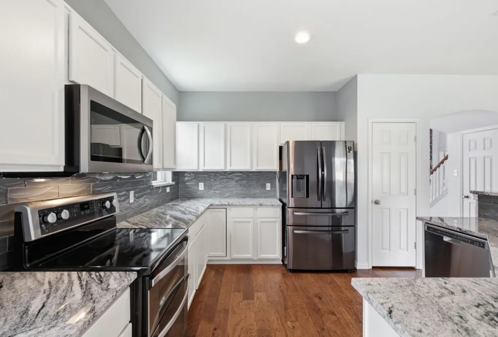 White cabinetry, stainless steel appliances, wood-finish flooring, stone countertops, and a tiled backsplash