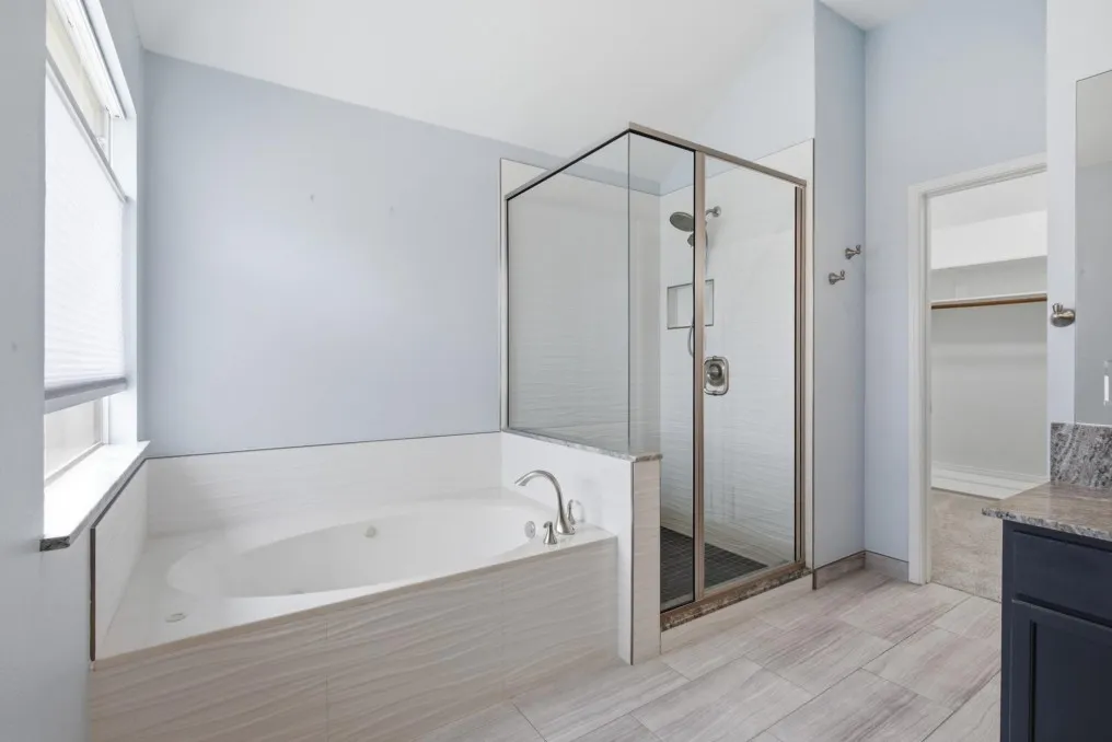 Soaking tub with tile surround, glass-enclosed shower, wood-finish flooring, and dark-toned vanity with stone countertop