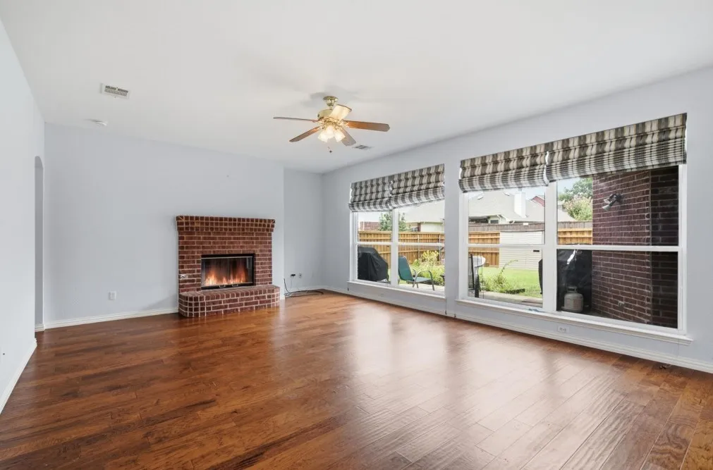 Wood-finish flooring, brick fireplace, multiple windows, and a ceiling fan with integrated lighting