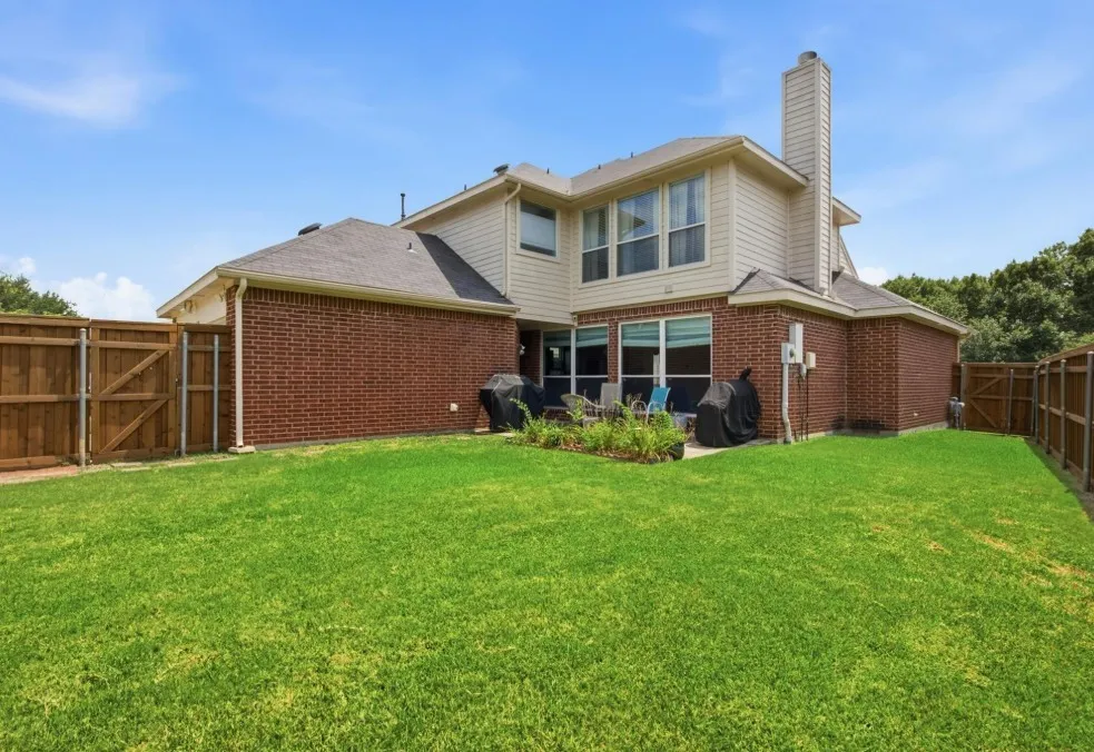 Expansive green lawn, brick and siding exterior, multi-pane windows, and a paved patio area