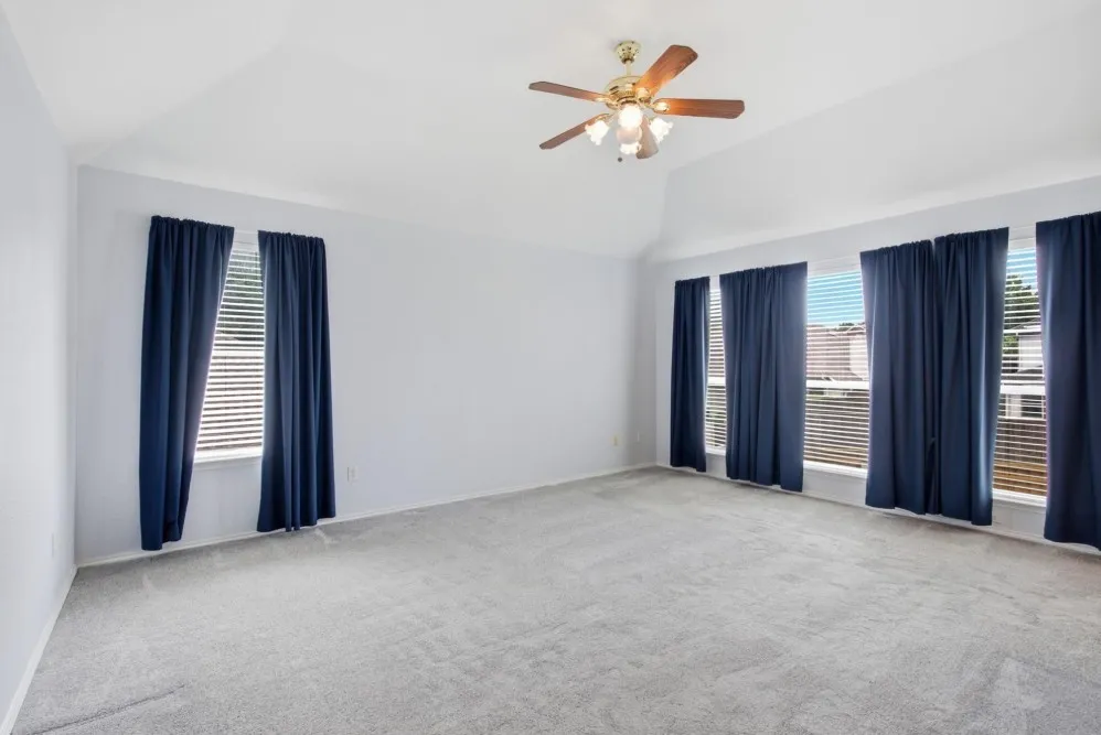 Vaulted ceiling with an attached ceiling fan, light gray carpeting, and multiple windows with blinds