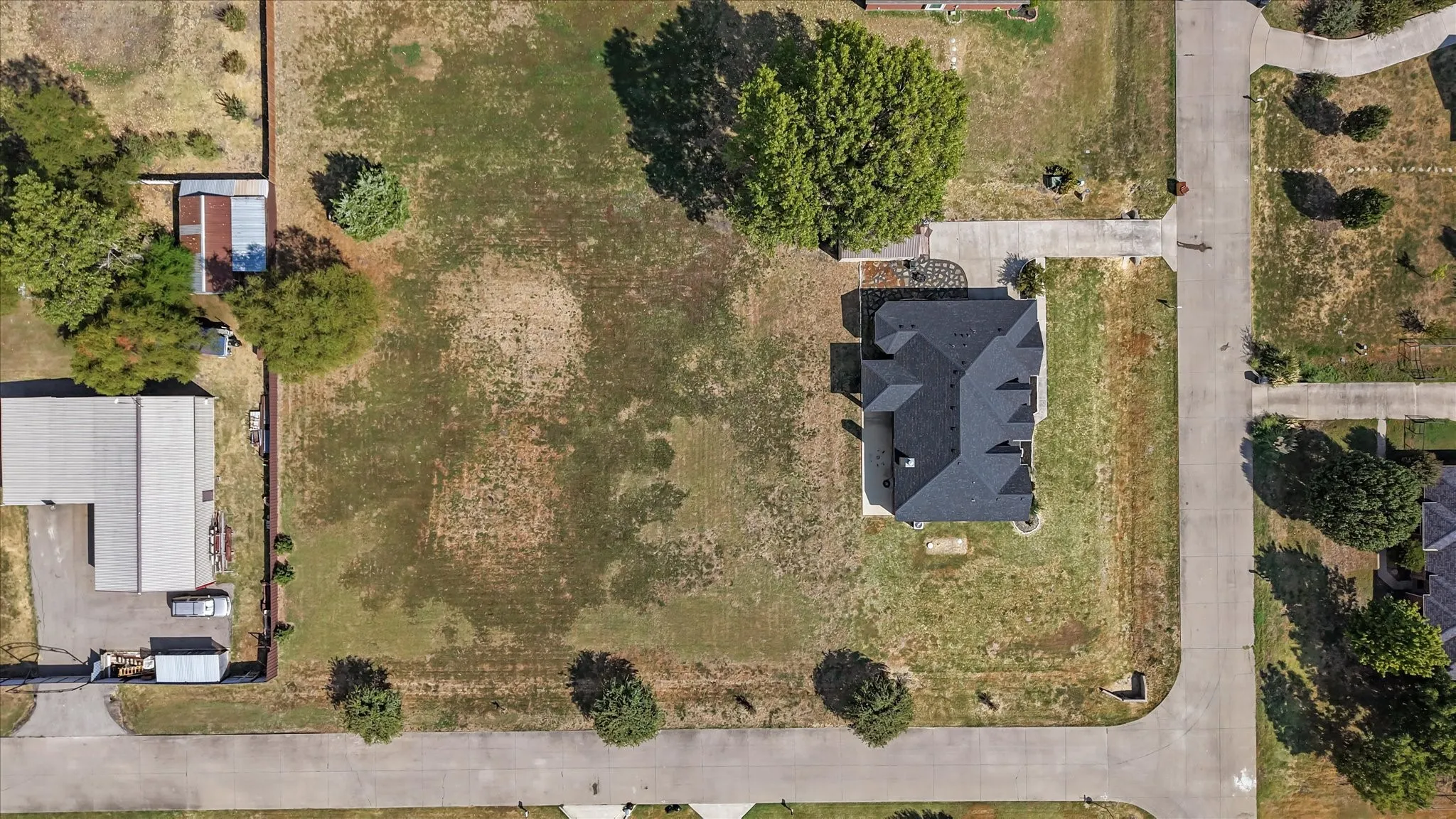 Aerial view showcasing a residential property with a dark shingle roof and extensive surrounding green space