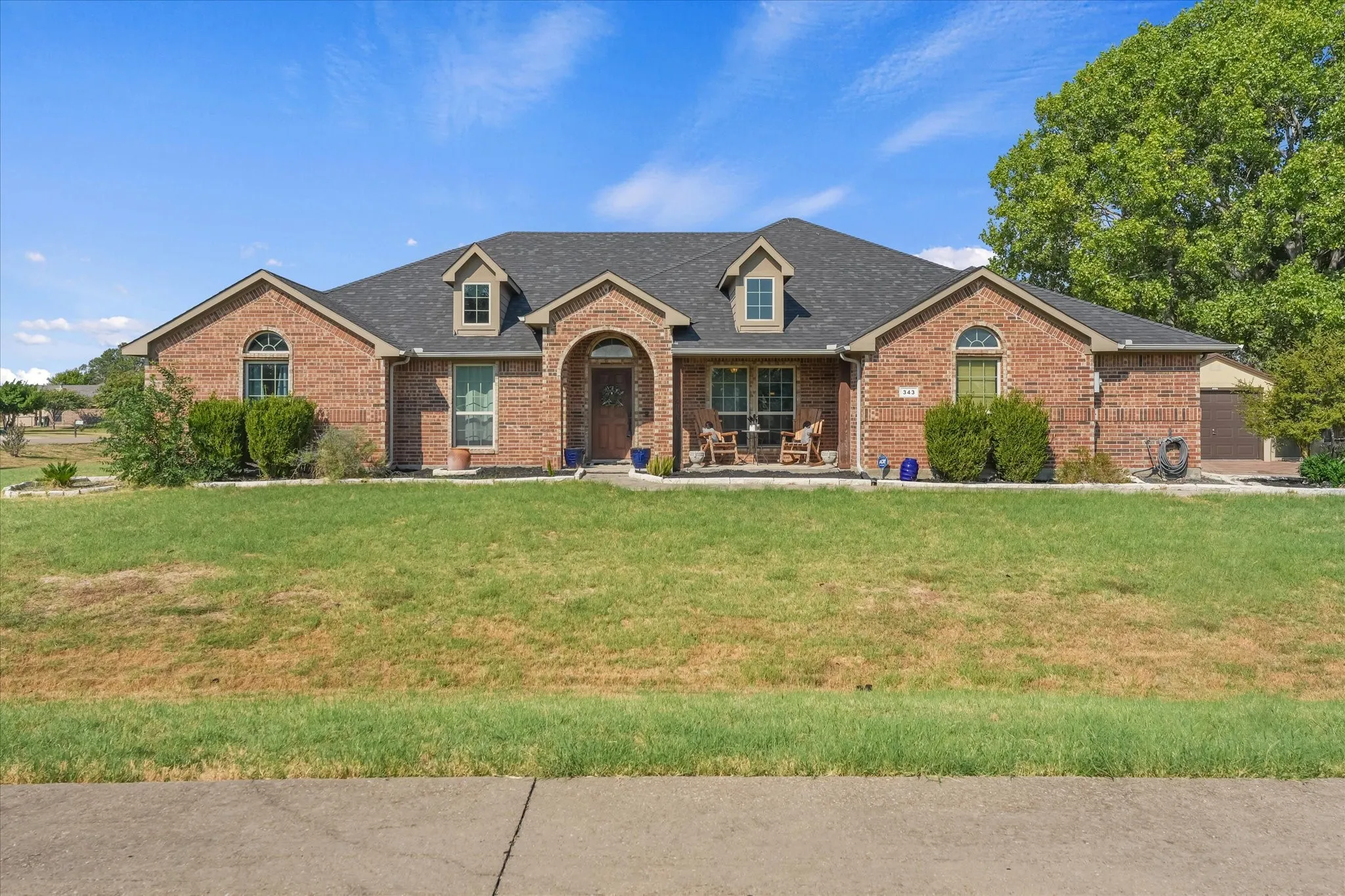 Brick exterior with an arched entry, dark shingle roof, and dormer windows, inviting front porch