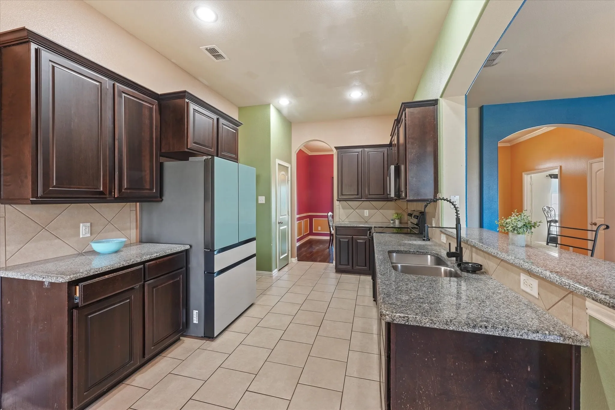 Kitchen featuring dark wood cabinetry, granite countertops, tile backsplash, and a double basin stainless steel sink with a black gooseneck faucet
