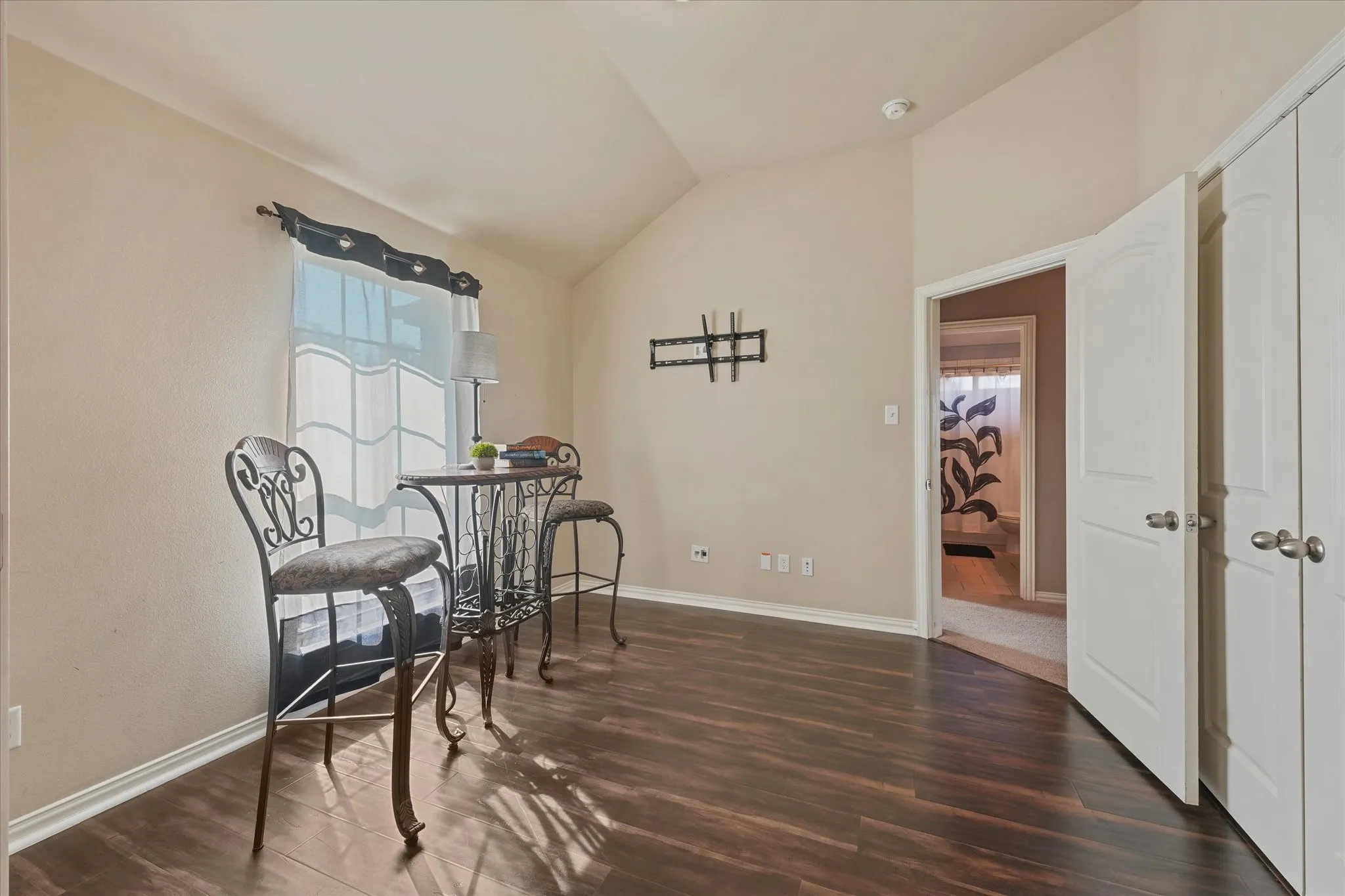 Vaulted ceiling, wood-finish flooring, window with natural light, white paneled doors, and a mounted tv bracket. Could be 5th bedroom