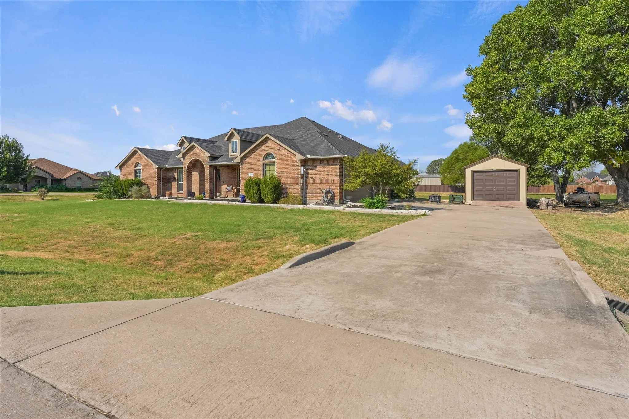 Brick exterior with arched entryways, dark shingle roof, attached garage, detached garage, and a concrete driveway