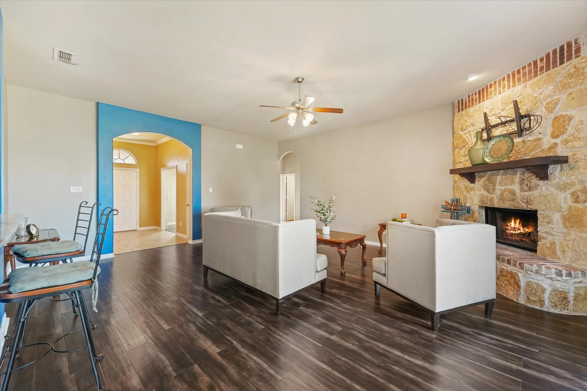 Stone-clad fireplace with wood mantle, wood-finish flooring, ceiling fan, and arched entryway