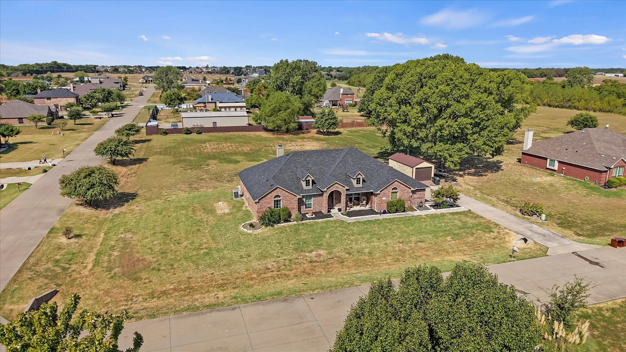 Brick exterior, dark shingle roof, attached dormer windows, landscaped front yard, detached storage shed