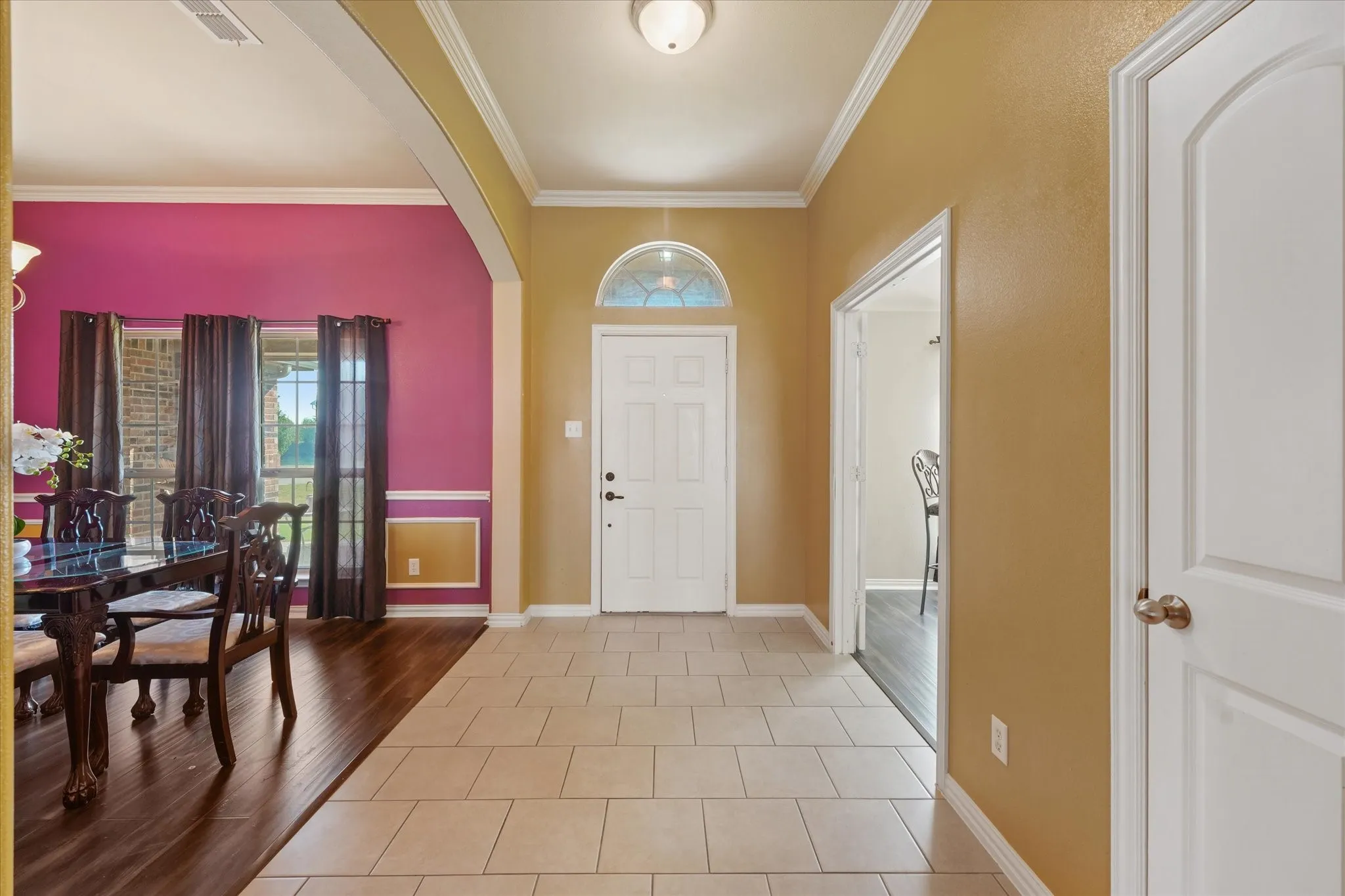 Entryway featuring light-toned tile flooring, a white paneled door with an arched transom window, and crown molding