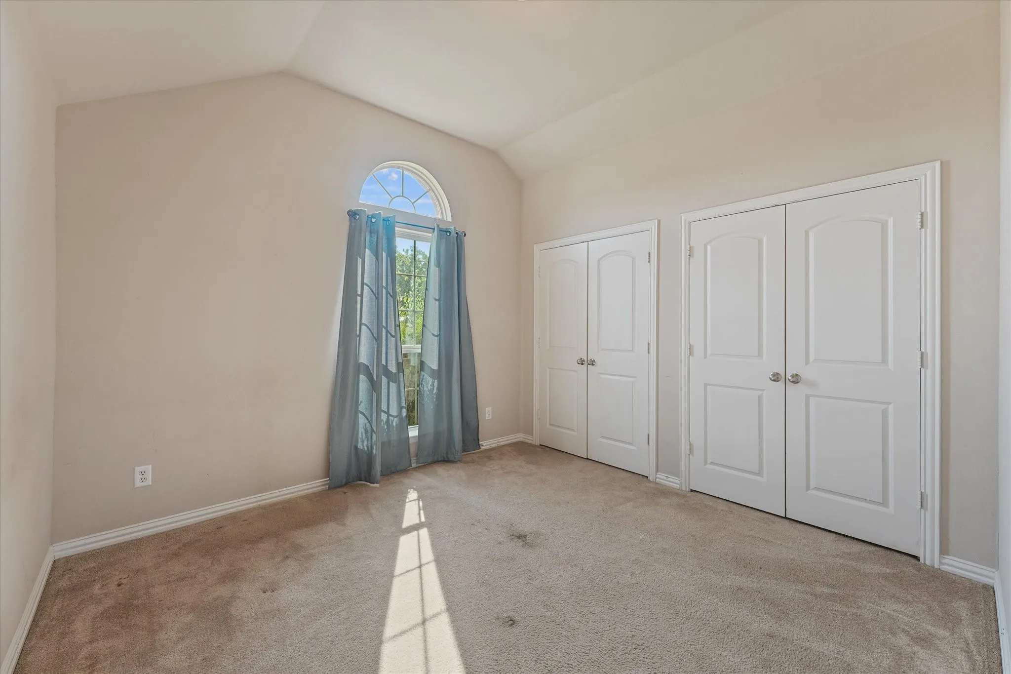 Vaulted ceiling, arched window, two sets of double closet doors, and neutral carpeting