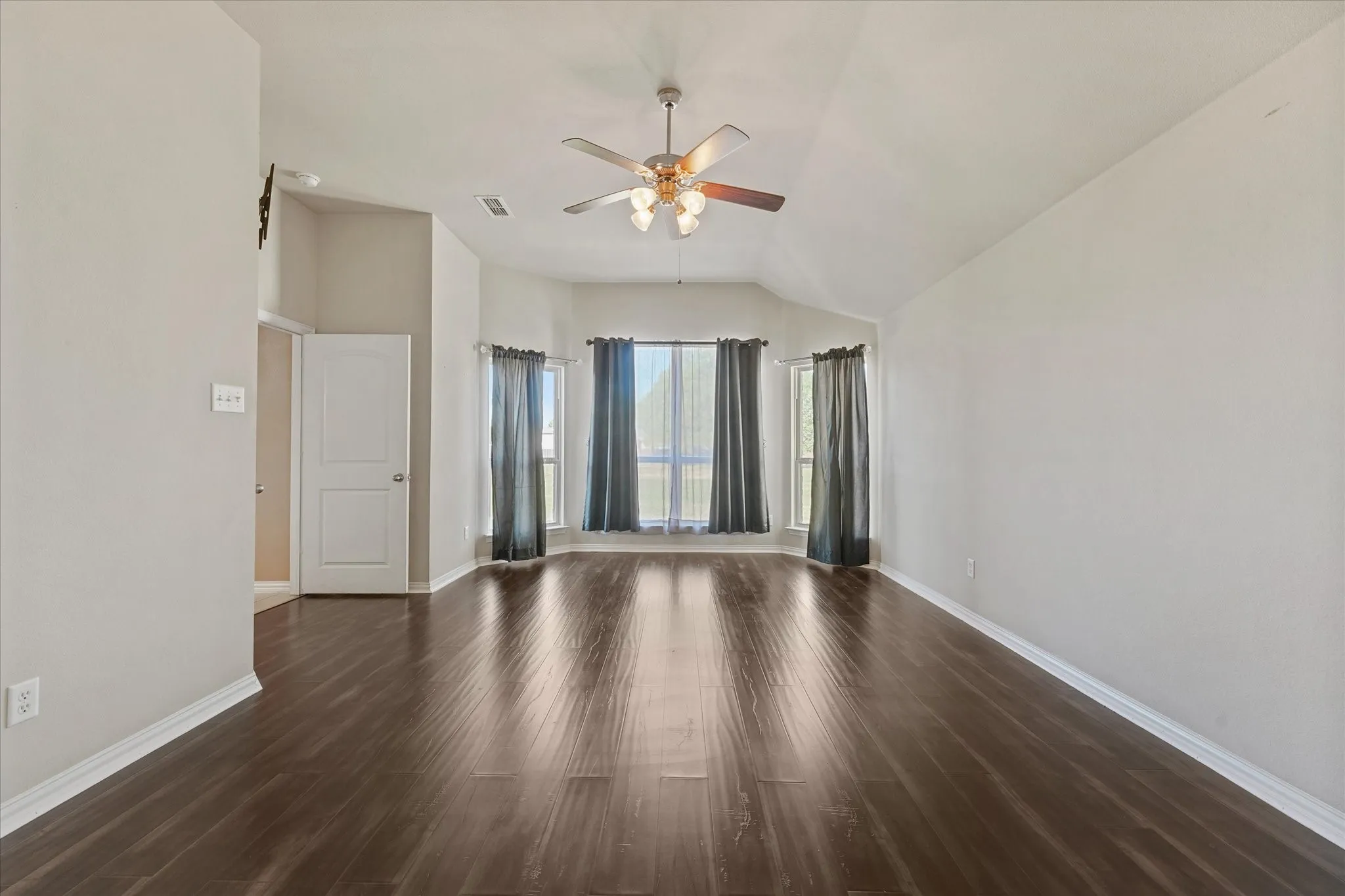 Vaulted ceiling with a ceiling fan, dark wood-finish flooring, and multiple windows with curtains