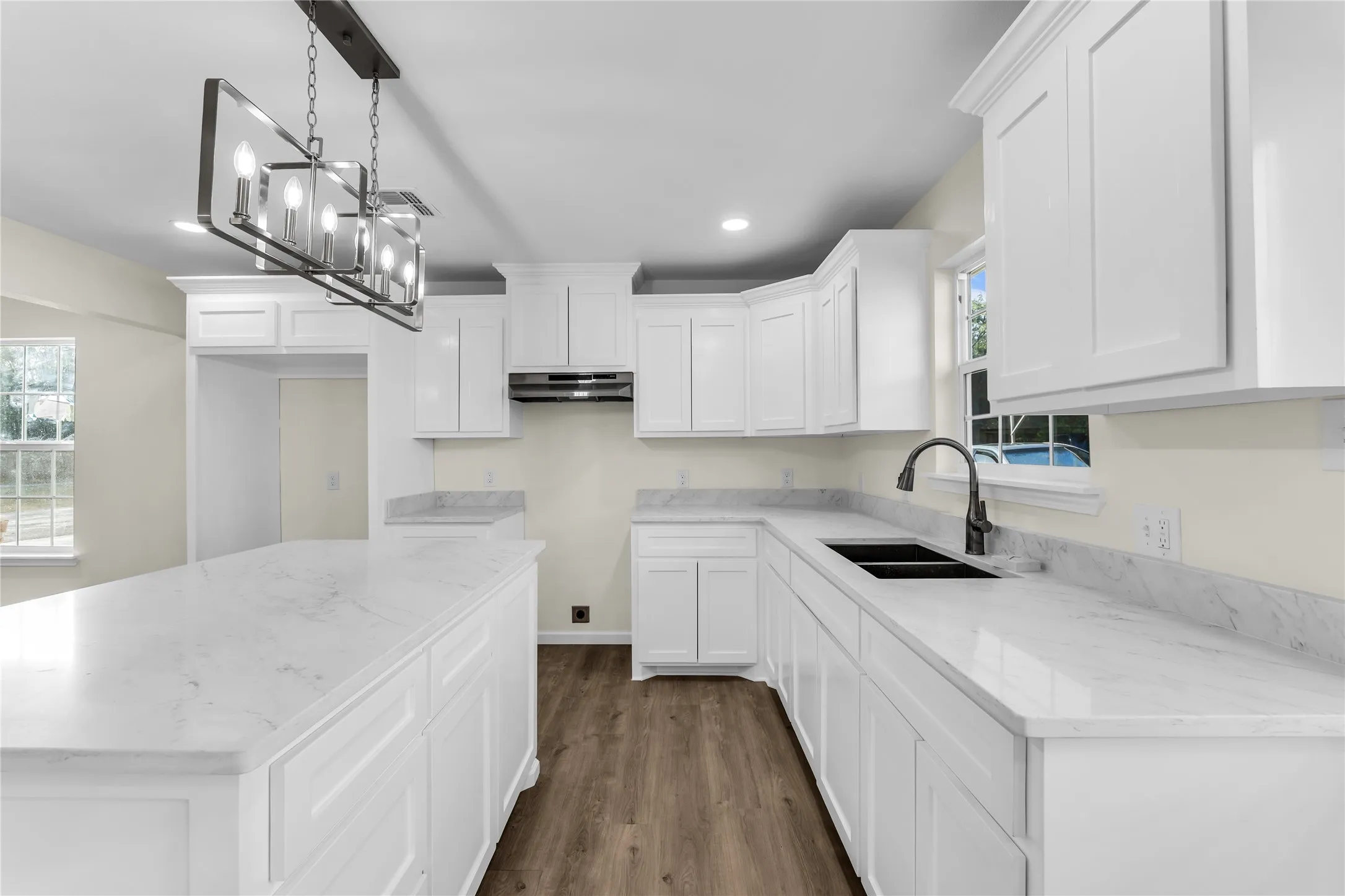 Spacious kitchen featuring white cabinetry, light countertops, wood-finish flooring, and a contemporary linear chandelier