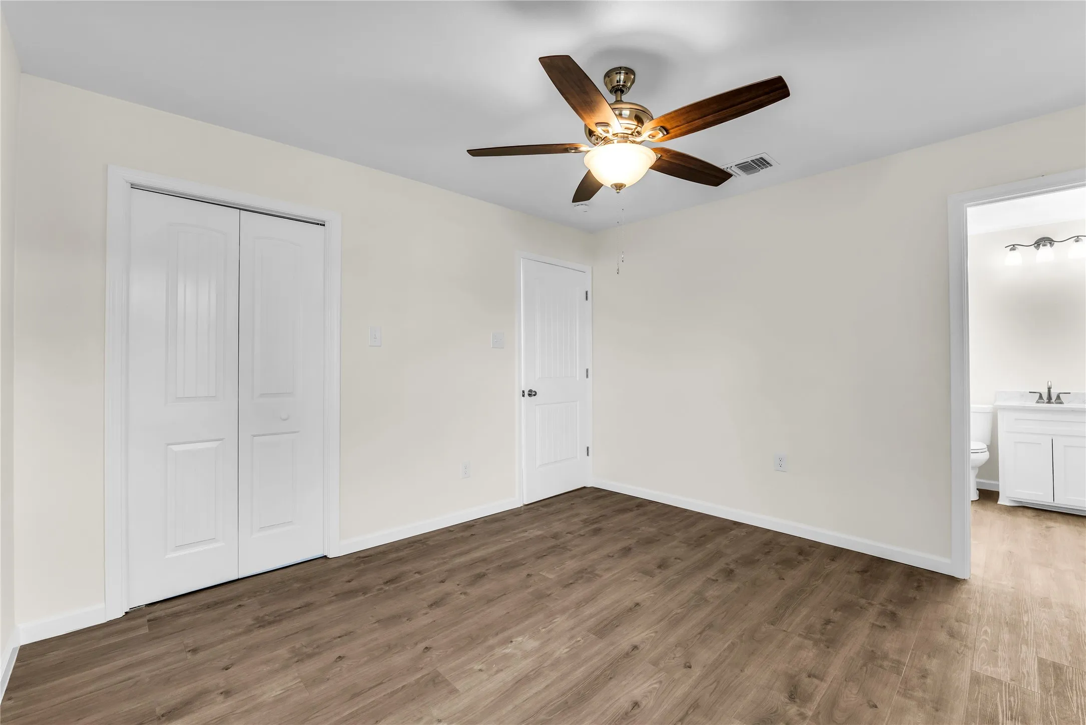 Wood-finish flooring throughout, bright white walls, and a ceiling fan with light fixture