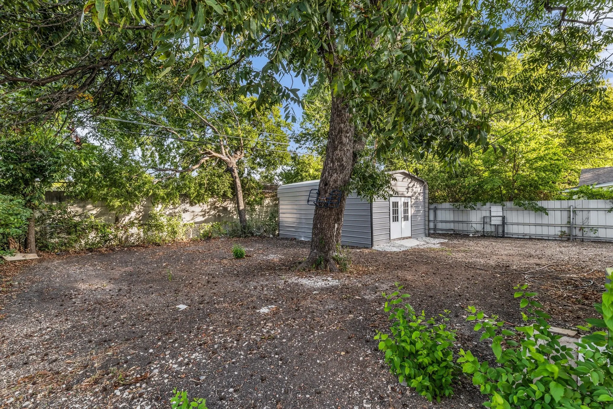 Spacious yard featuring a large tree, a detached utility shed with double doors, and perimeter fencing
