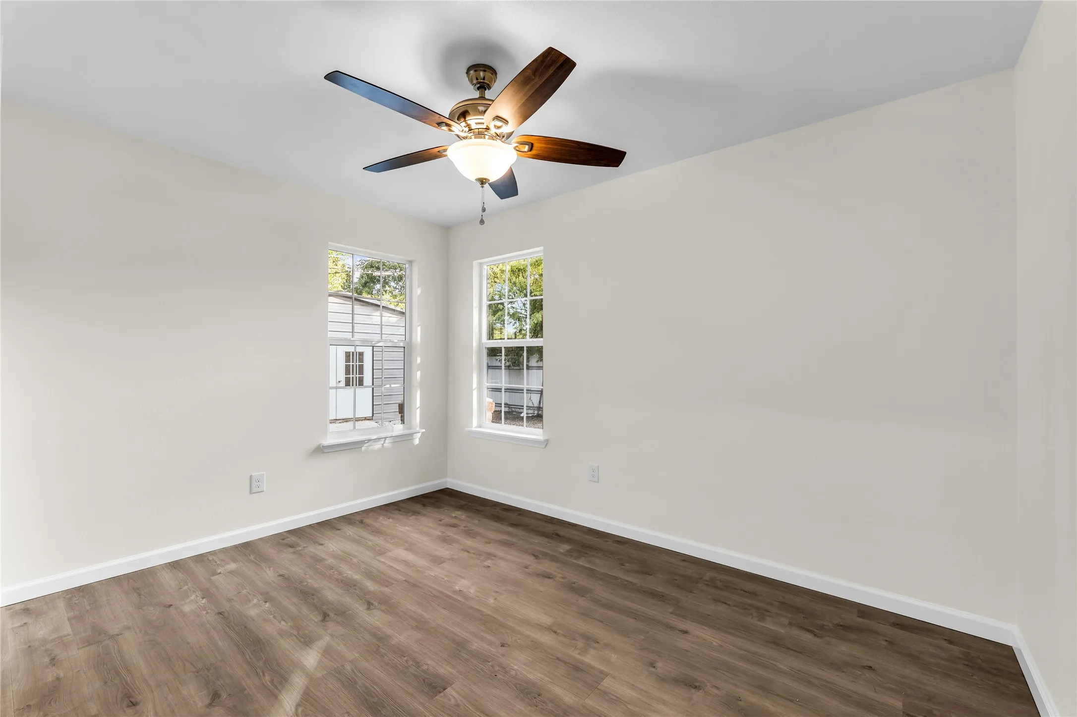 Neutral wall color, wood-finish flooring, two windows, and a ceiling fan with integrated lighting