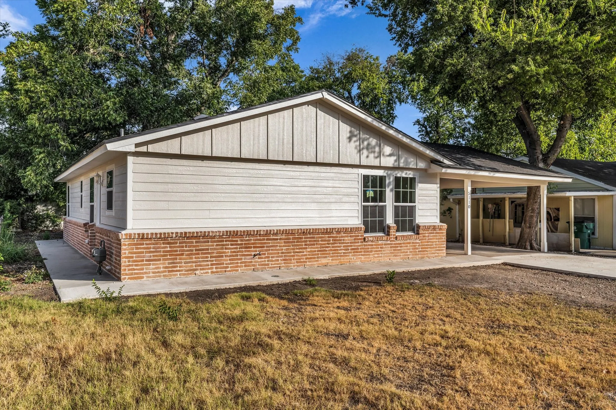Exterior featuring brick wainscoting, light-colored siding, and a covered carport with structural support
