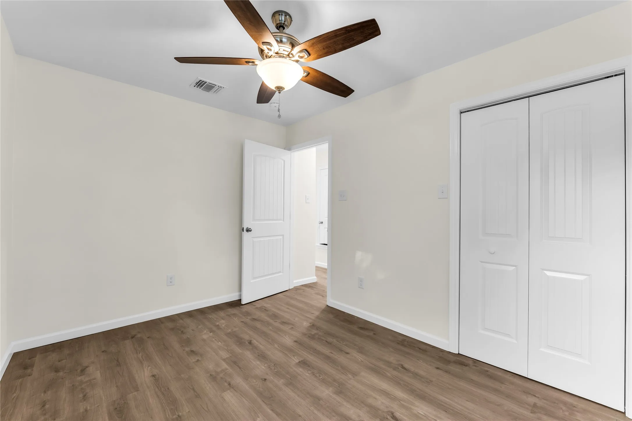 Wood-finish flooring with white baseboards, a ceiling fan with light fixture, and white bi-fold closet doors