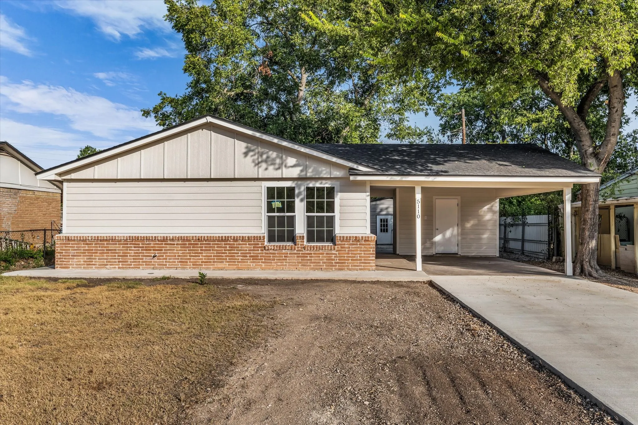 Exterior featuring brick wainscoting, light-colored siding, a carport, and a concrete driveway