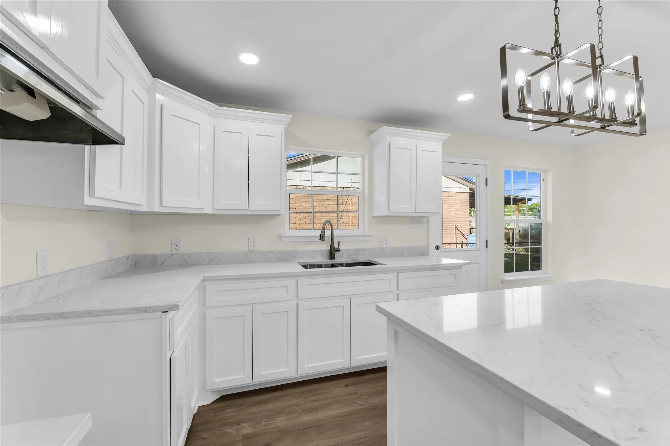 White shaker cabinetry with crown molding, light-toned countertops, a central island, wood-finish flooring, and a contemporary chandelier