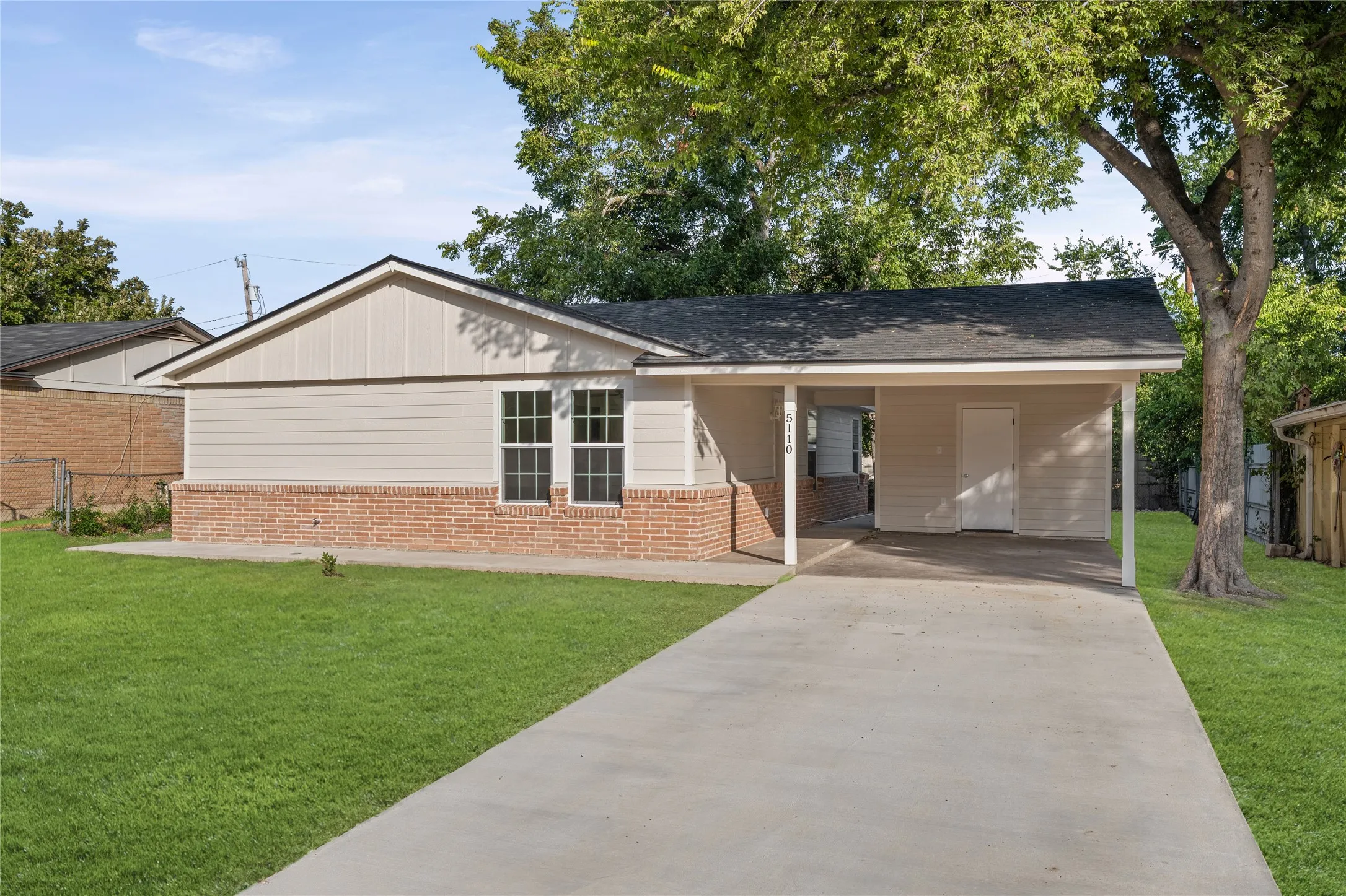 Exterior featuring brick wainscoting, light-colored horizontal siding, and a covered carport with a concrete driveway