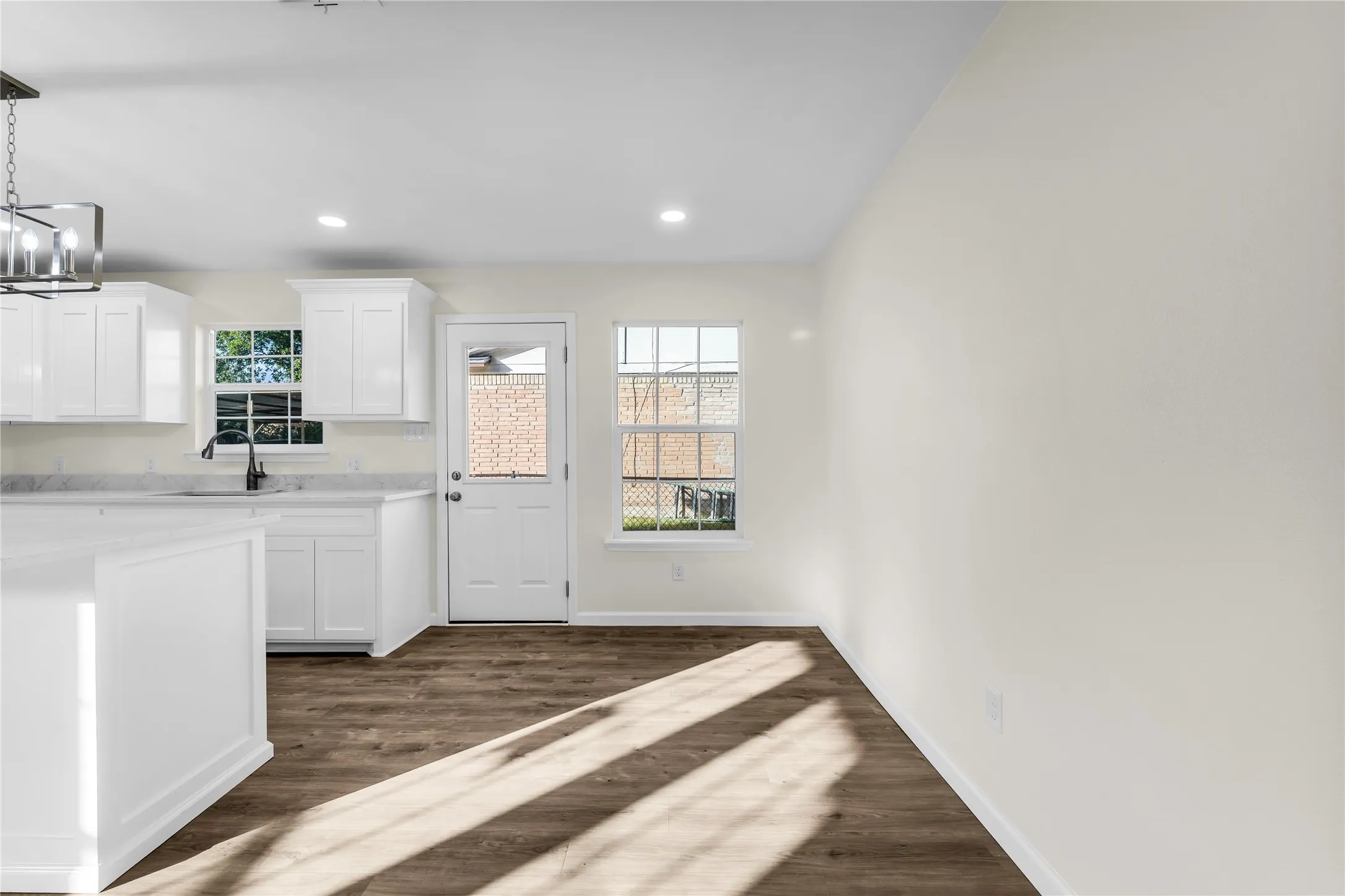 Open-concept living space with wood-finish flooring, white cabinetry, recessed lighting, and a modern chandelier
