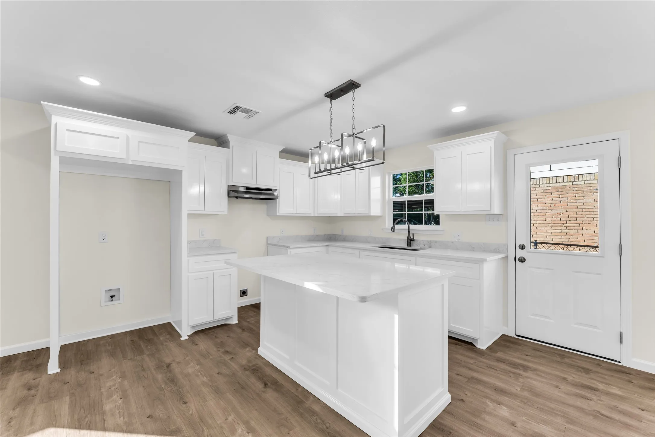 White kitchen cabinetry, center island with solid surface countertop, wood-finish flooring, recessed lighting, and a modern rectangular chandelier