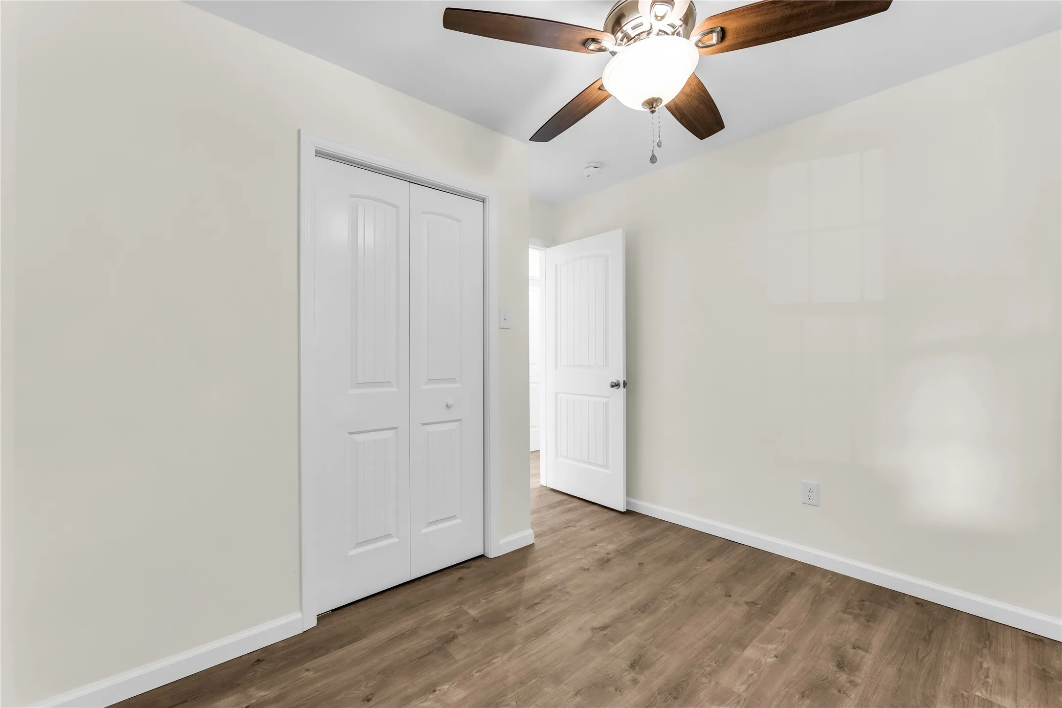 Wood-finish flooring, white walls, and a ceiling fan with integrated lighting