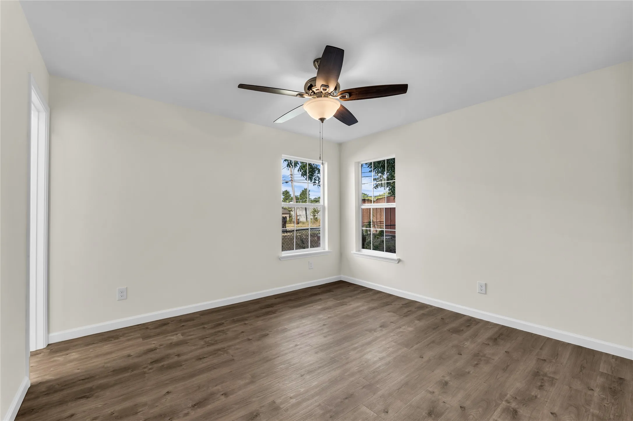 Wood-finish flooring, two windows with white trim, a ceiling fan with integrated lighting, and neutral wall tones