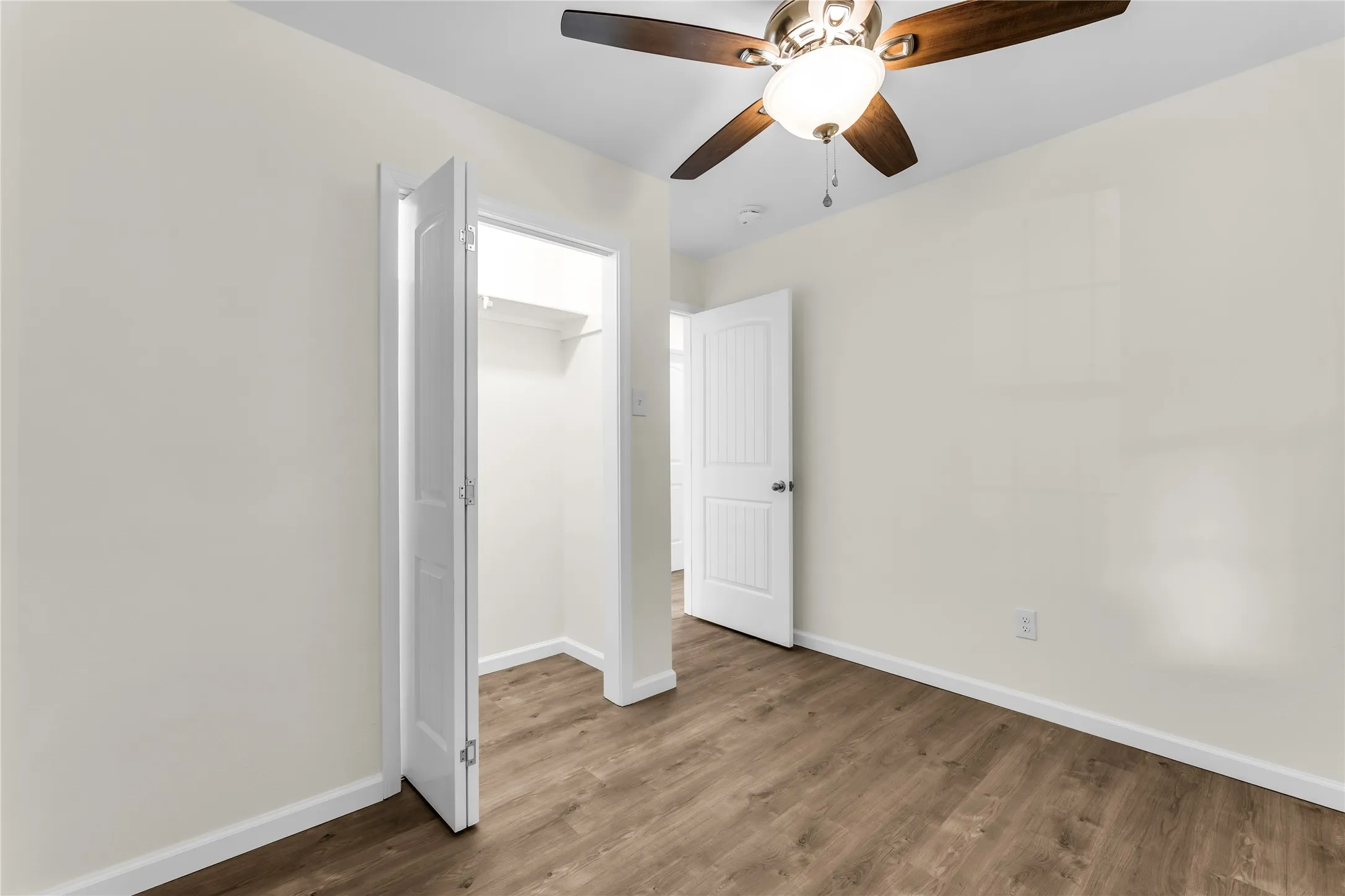 Wood-finish flooring, ceiling fan with integrated lighting, and a bi-fold closet