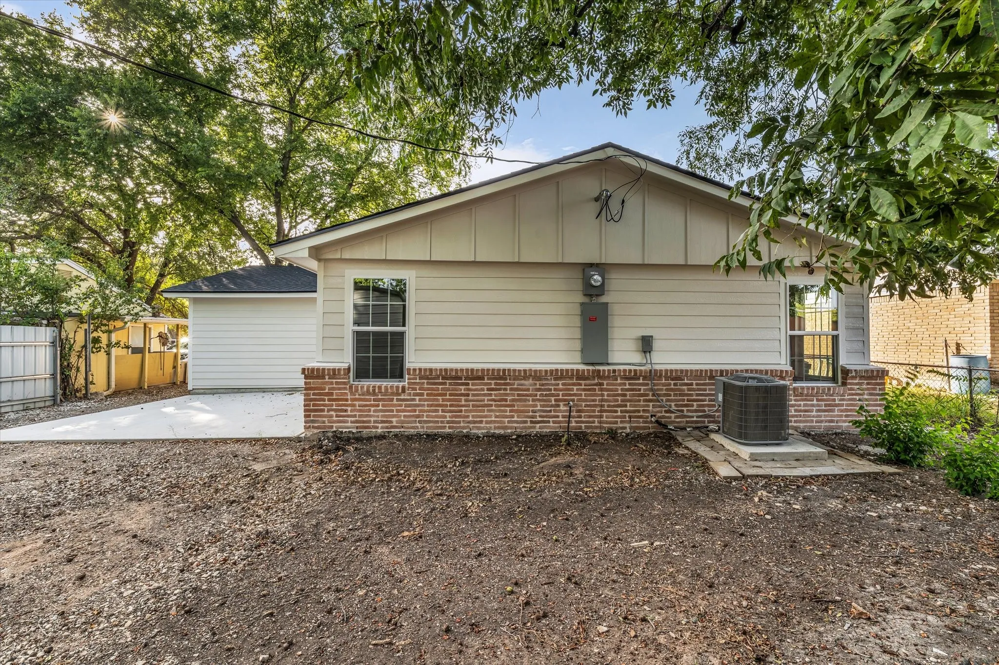 Rear exterior with light-colored siding, brick accent, and a newly poured concrete pad