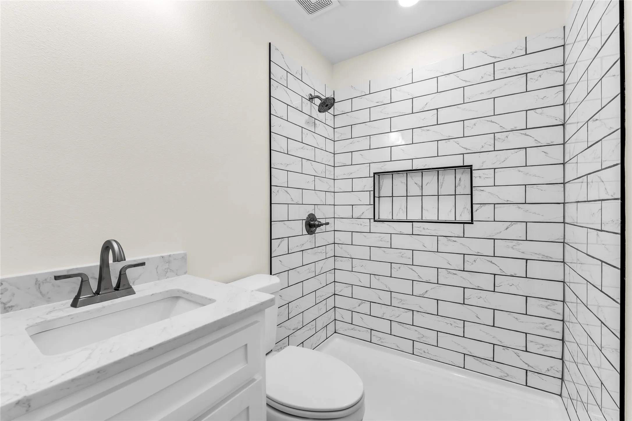 White subway tile shower surround with integrated niche, matte black shower fixtures, vanity with integrated white sink and counter, and matte black faucet