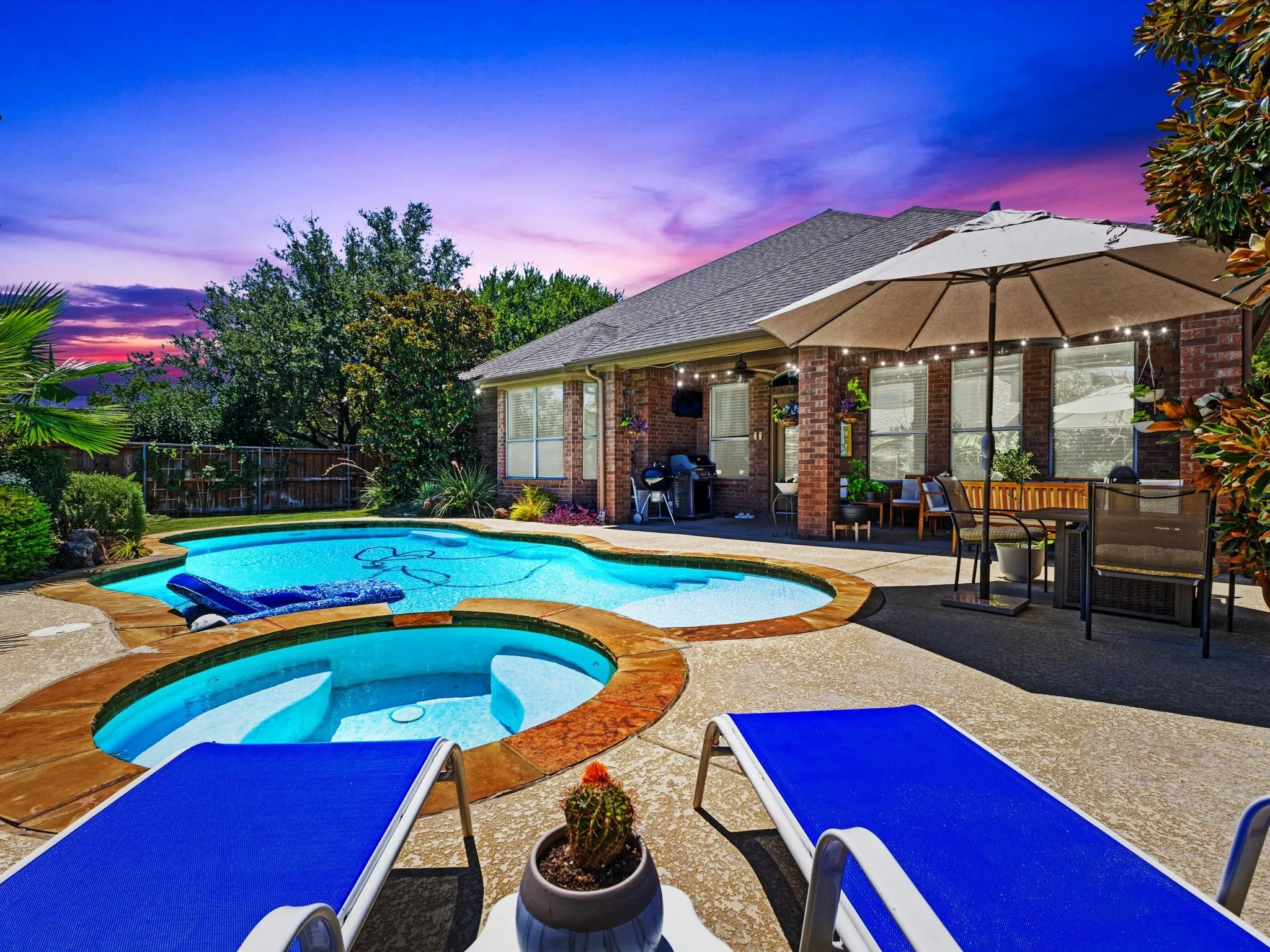 Expansive concrete patio featuring a built-in pool and hot tub, surrounded by mature landscaping