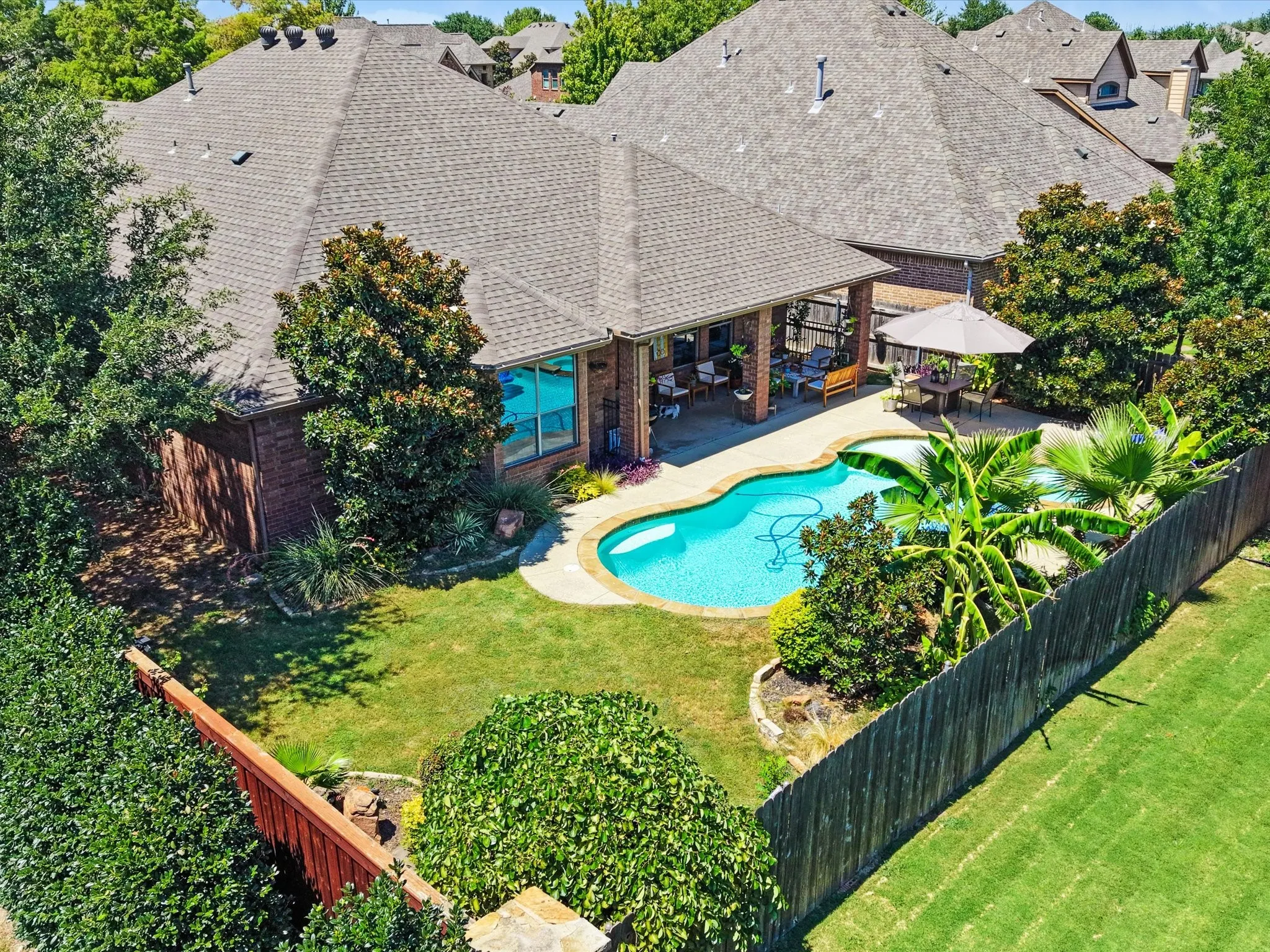 Brick exterior, covered patio, freeform swimming pool, concrete pool decking, and mature landscaping