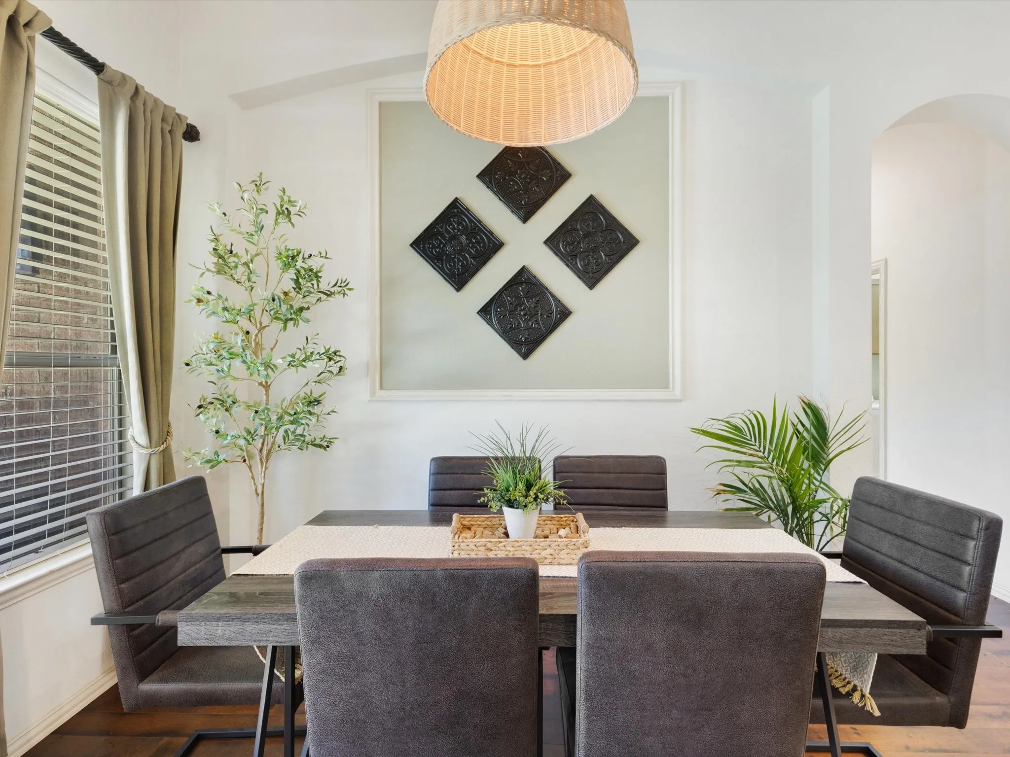 Wood-finish flooring, window with horizontal blinds, arched doorway, and a woven pendant light fixture