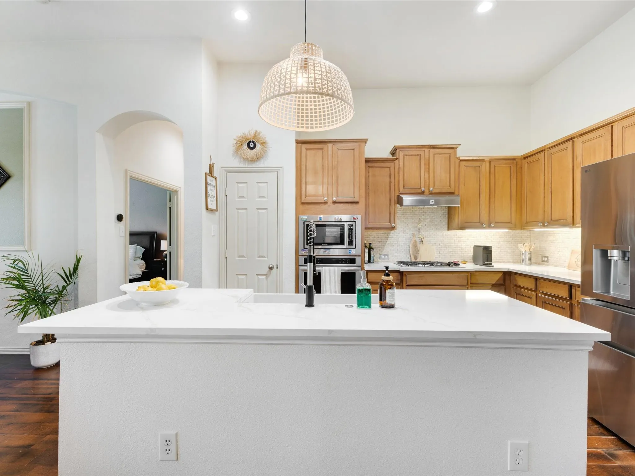 Kitchen featuring a large island with a white countertop, wood-finish cabinetry, stainless steel appliances, and a decorative pendant light fixture