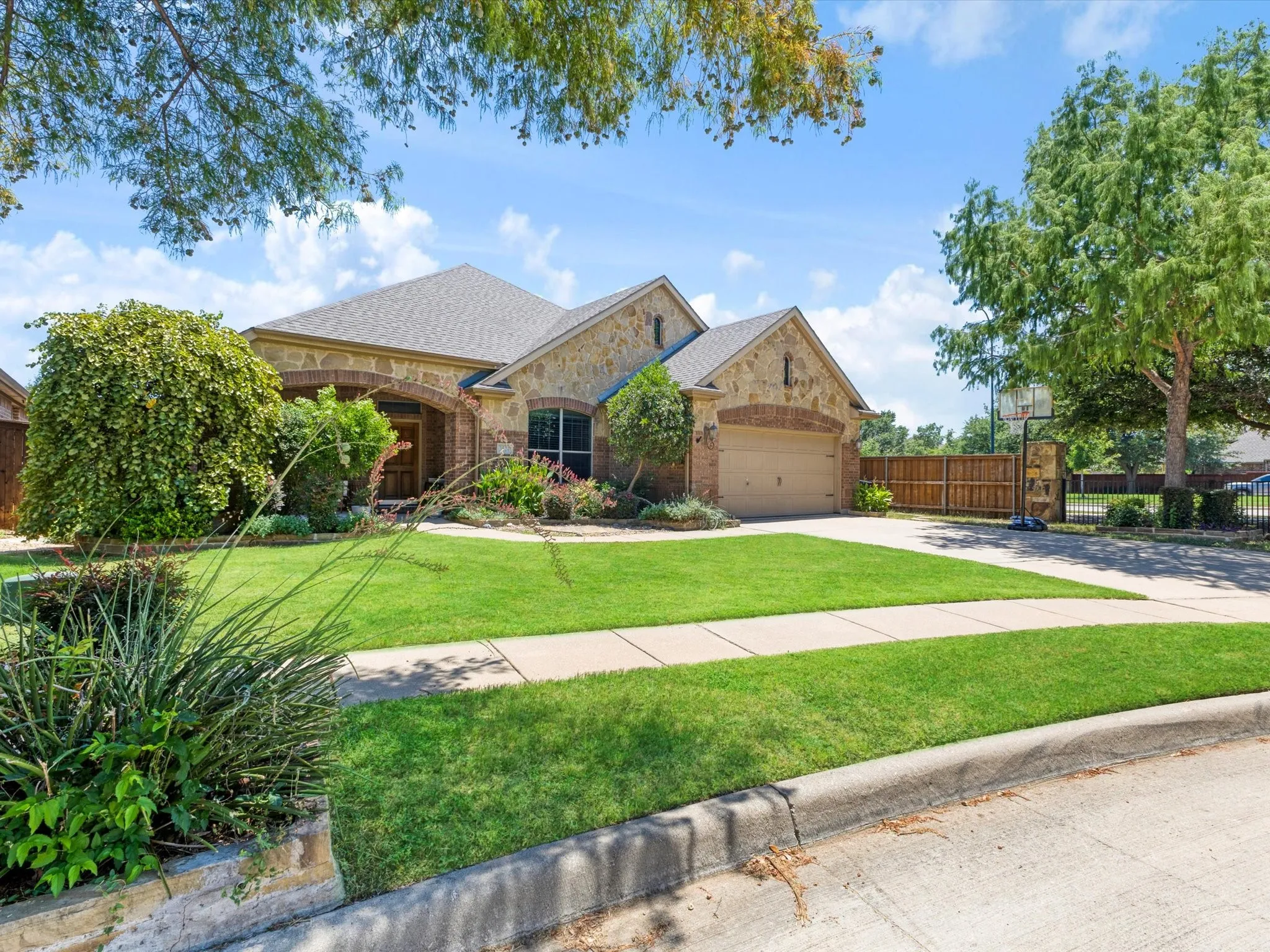 Stone and brick exterior with arched entryway, attached garage, and mature landscaping