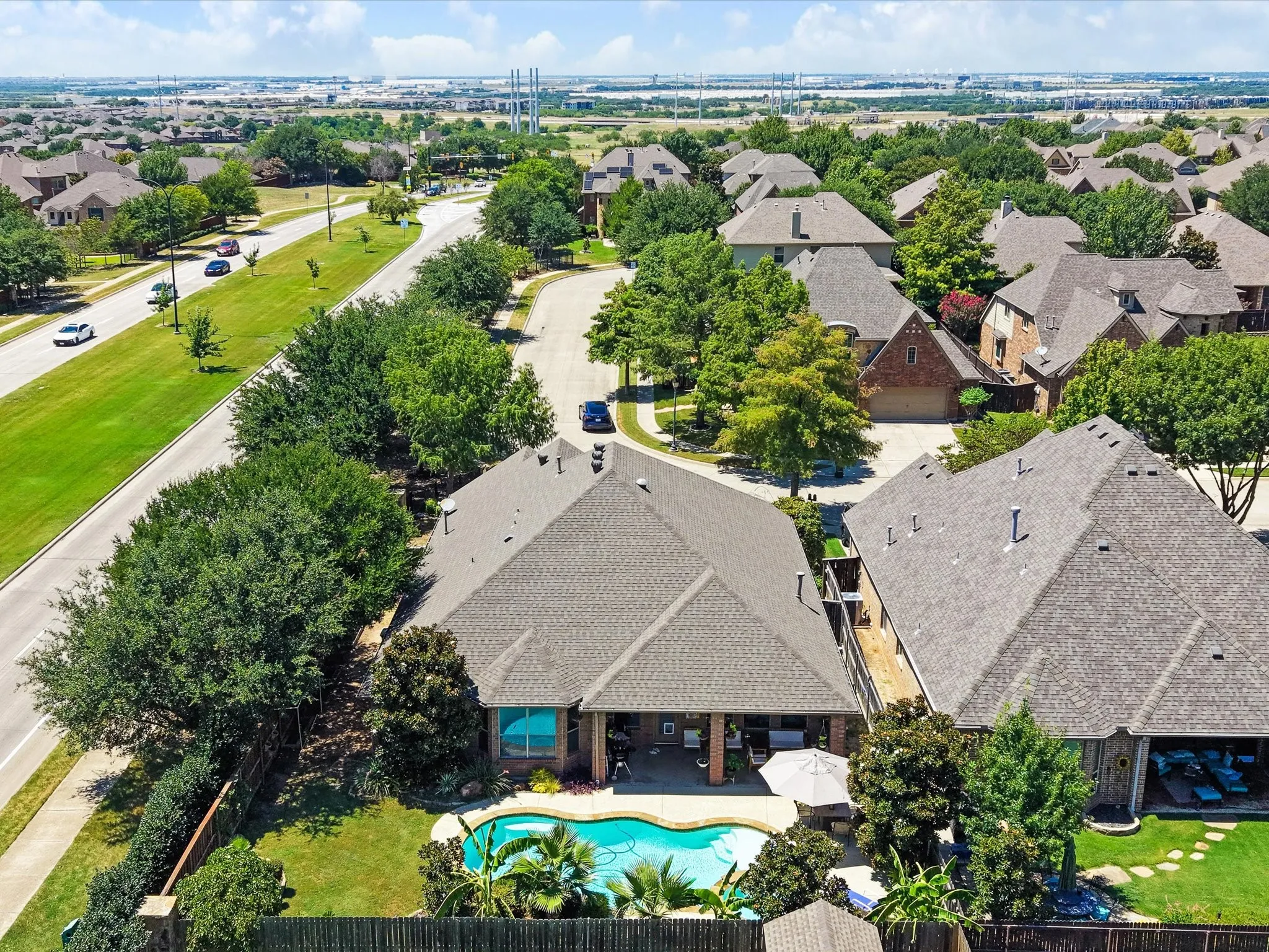 Backyard oasis featuring a curvilinear swimming pool, covered patio, wood fencing, and mature landscaping