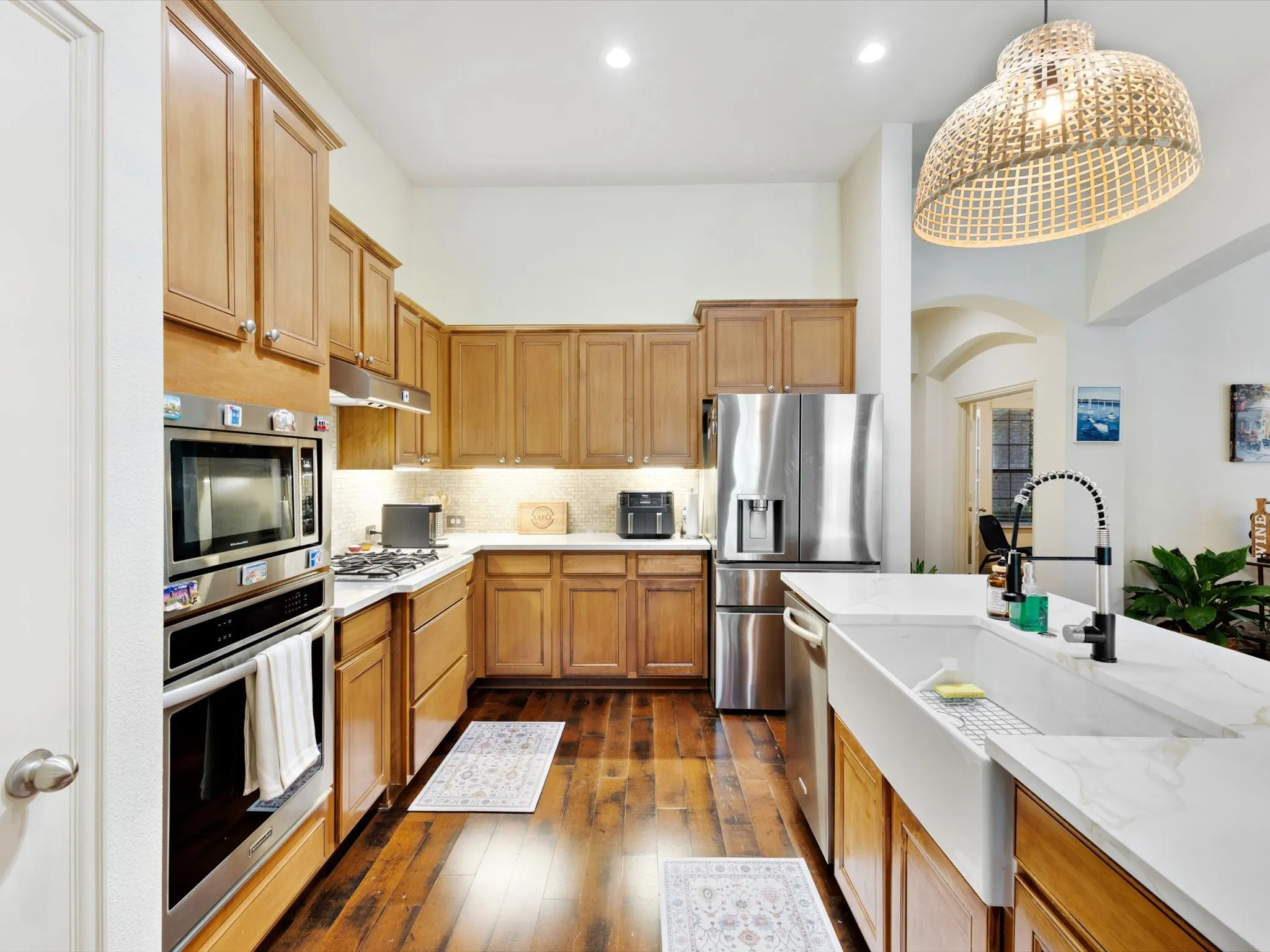 Gourmet kitchen featuring wood-finish flooring, stainless steel appliances, a farmhouse sink, and light-toned cabinetry
