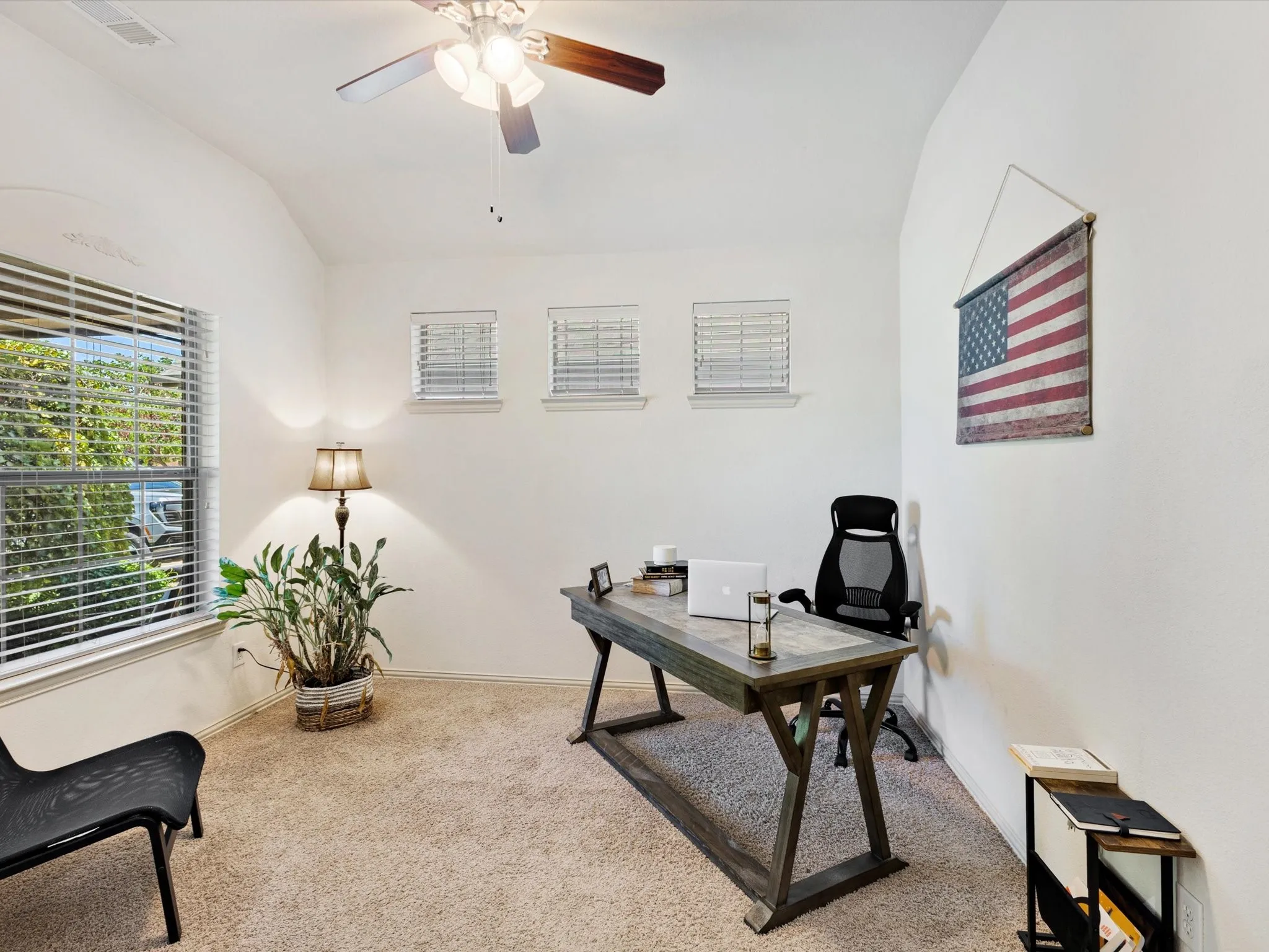 Light-toned carpeting, multiple windows with blinds, and a built-in ceiling fan with integrated lighting
