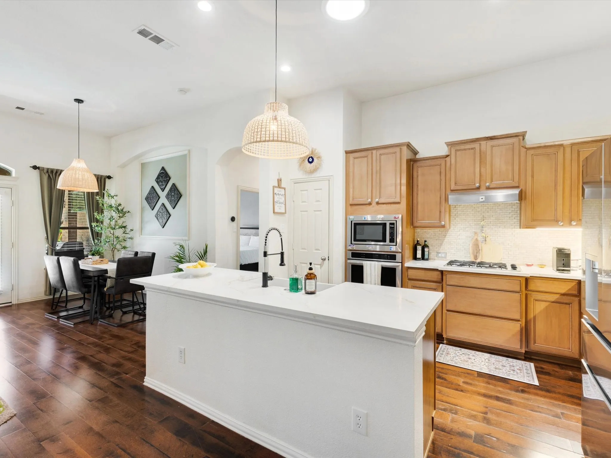 Kitchen featuring a central island with a white countertop, wood-finish flooring, light wood cabinetry, stainless steel appliances, and a tile backsplash