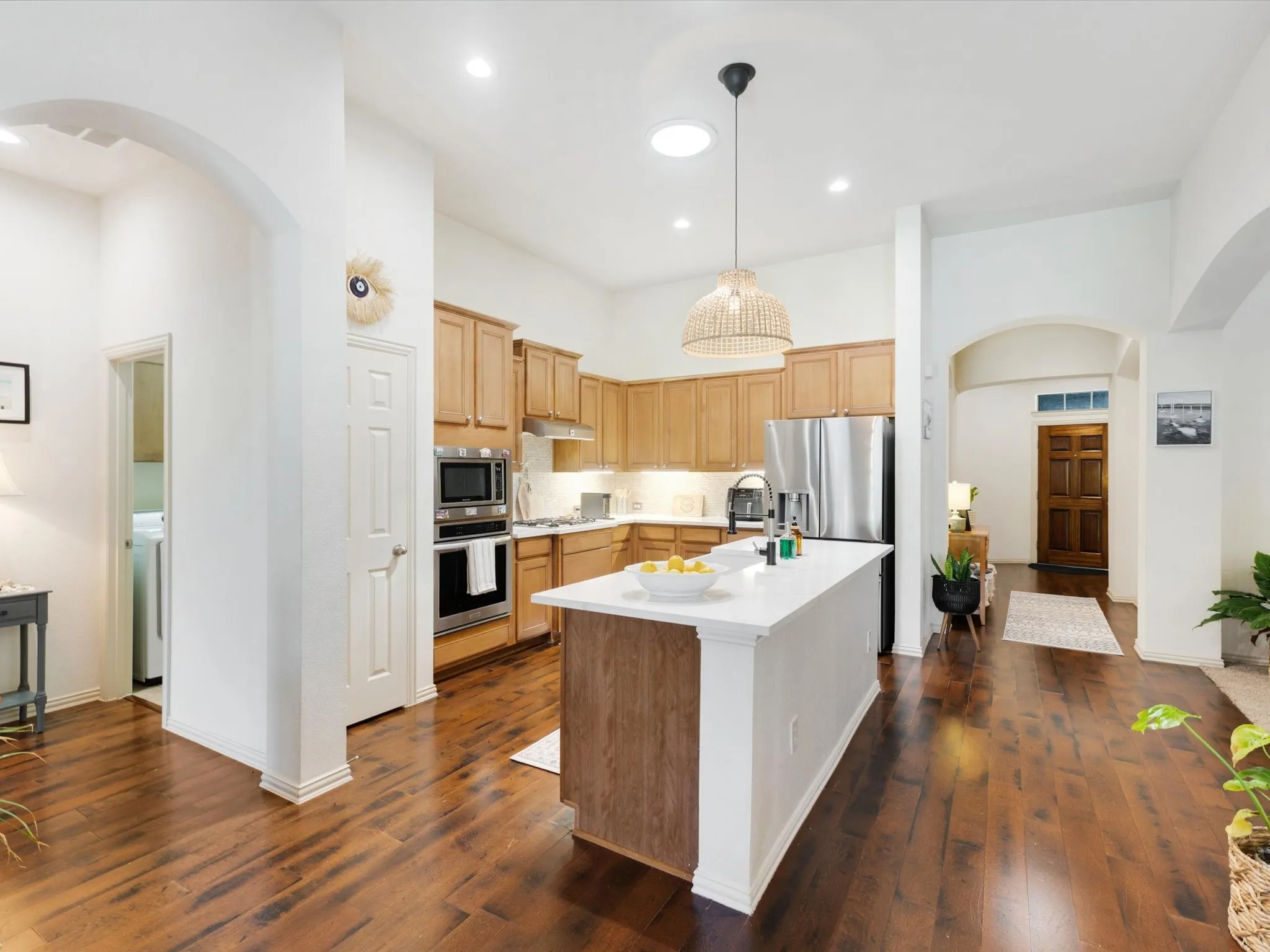 Gourmet kitchen with wood-finish flooring, light wood cabinetry, stainless steel appliances, a center island with a white countertop, and recessed lighting