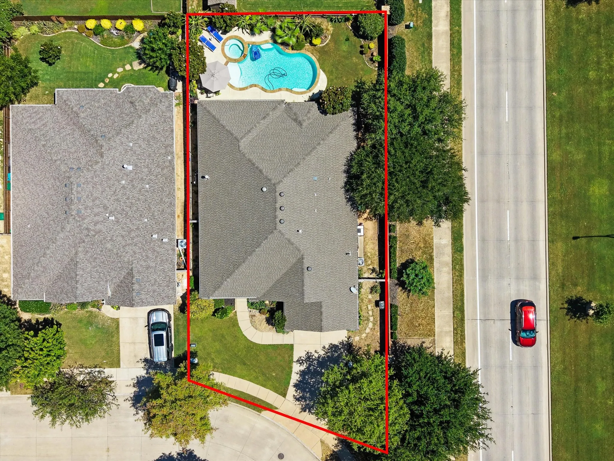 Property featuring a pool, an integrated spa, an adjacent patio area, a paved driveway, and mature landscaping