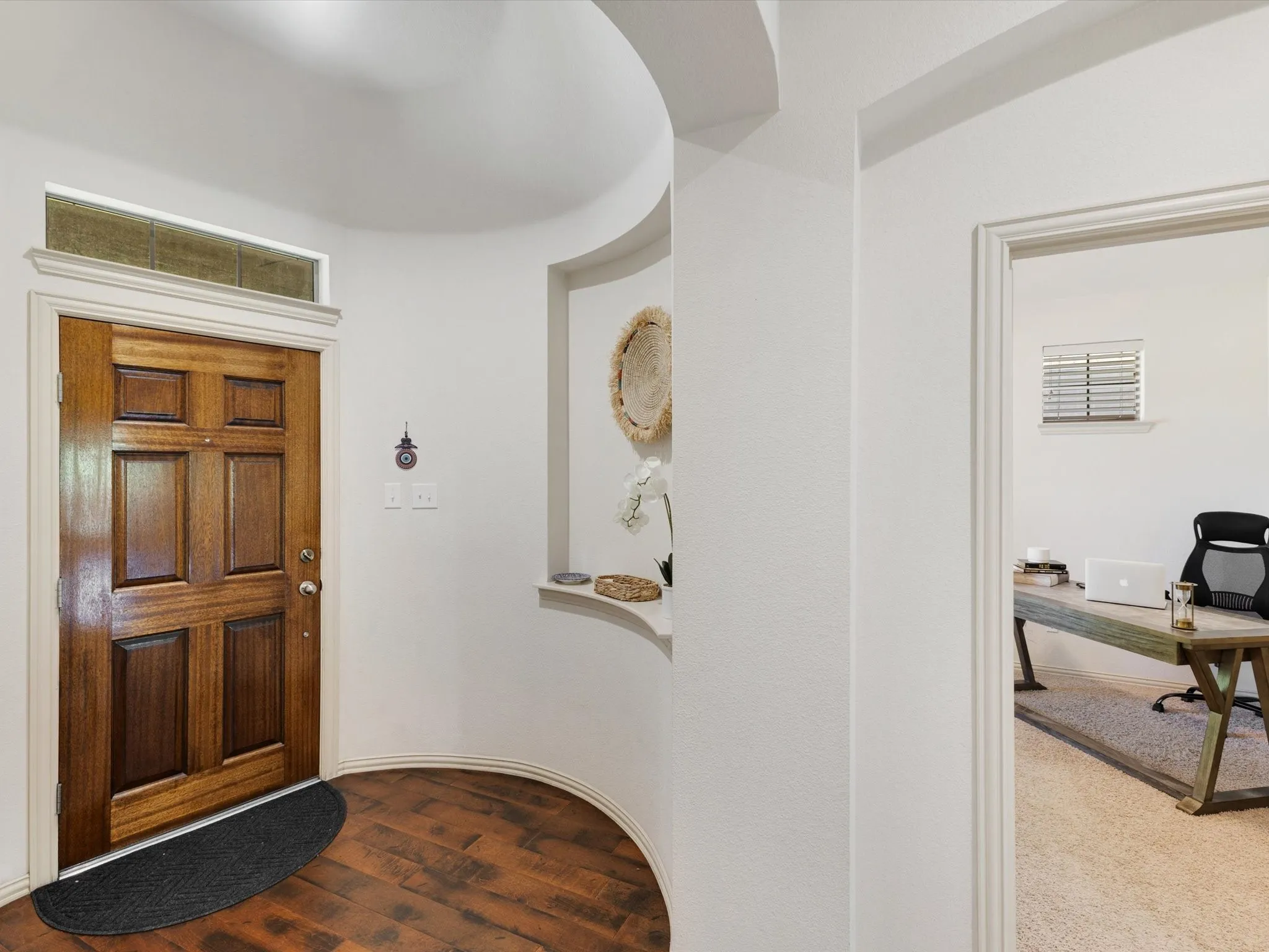 Solid wood entry door with transom window, wood-finish flooring, architectural archway, and built-in wall niche